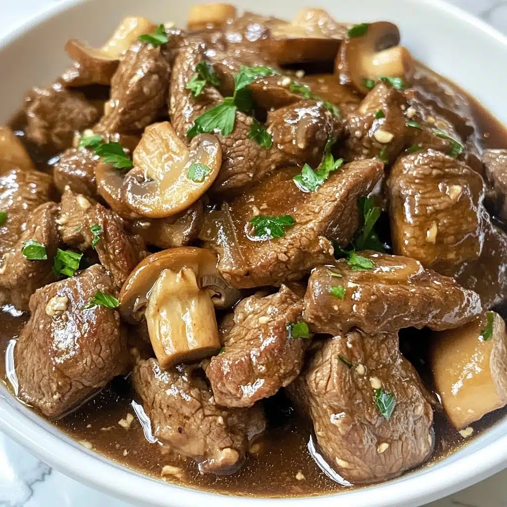 Instant Pot Garlic Butter Steak Bites, garlic butter steak bites, instant pot steak dinner, quick steak recipes, tender beef bites The dish shows small brown pieces of cooked meat mixed with sliced mushrooms and bits of garlic, all covered in a thin brown sauce. It is garnished with small green parsley leaves scattered on top. The food is served in a white bowl, sitting on a white marbled surface. The close-up angle reveals the texture of the meat and mushrooms clearly.