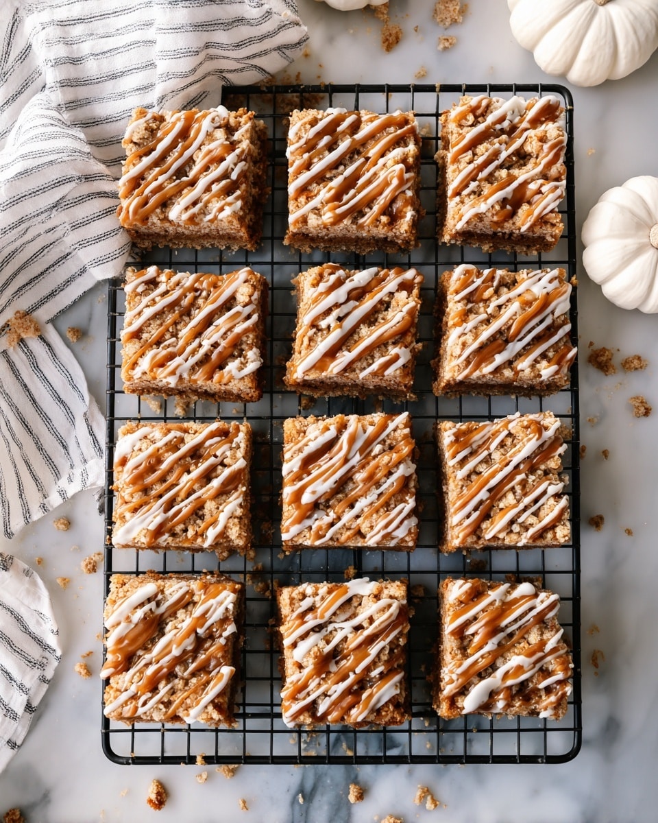 There are sixteen square dessert bars arranged in a 4x4 grid on a black cooling rack. Each bar has three visible layers: a golden brown base, a lighter crumbly middle layer, and a crumbly top layer. The top is decorated with drizzles of caramel and white icing, creating a striped pattern across each bar. The bars sit on a white marbled surface with scattered crumbs and a white and gray striped cloth partially visible on the left. Two small white pumpkins appear faintly in the upper right corner. Photo taken with an iphone --ar 4:5 --v 7