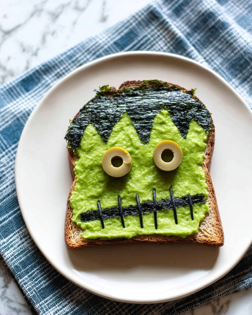 A piece of toast with three layers sits on a white plate on top of a blue and white checked cloth. The bottom layer is a brown, crispy toasted bread. The middle layer is a smooth spread of bright green avocado covering the entire surface of the toast. The top layer is made from dark green seaweed shaped with a zigzag edge representing hair along the top part. Two light green olive slices are placed near the center, resembling eyes. Thin strips of the dark green seaweed form a stitched mouth below the eyes, creating a face. The background features a white marbled surface. Photo taken with an iphone --ar 4:5 --v 7