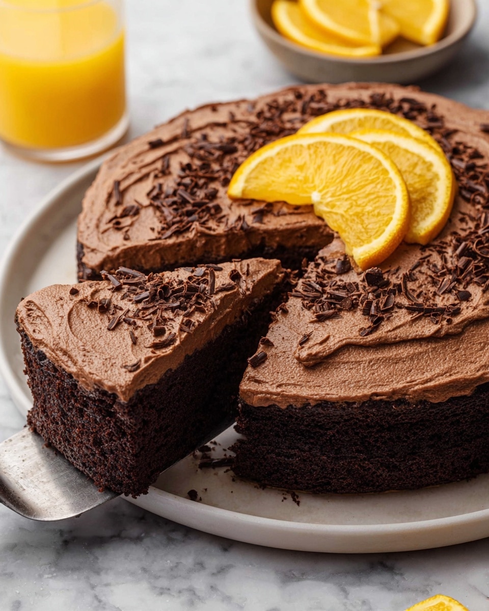 A round chocolate cake with two visible layers, a dense dark chocolate base, and a thick, creamy chocolate frosting layer on top that is swirled with a slightly rough texture. The cake is placed on a white plate. The top is decorated with curled dark chocolate shavings and several bright orange slices arranged in a fan shape on one side. One slice of the cake is slightly pulled out, revealing the rich inside. Around the plate, there are extra orange slices and a clear glass filled with orange juice on a white marbled surface. photo taken with an iphone --ar 4:5 --v 7