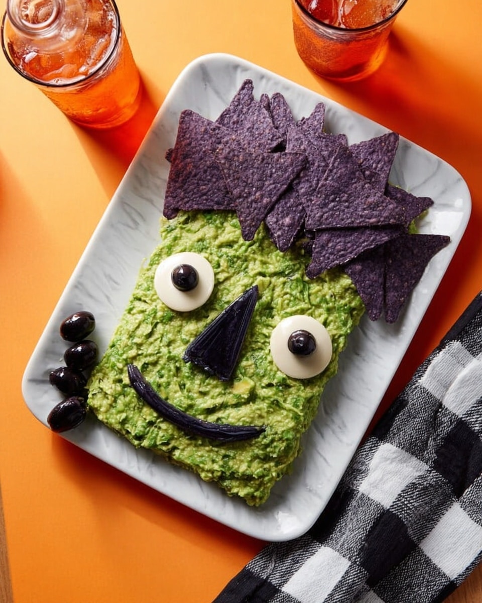 The dish is shaped like a funny face on a white rectangular plate. The base layer is green and smooth, like a thick spread, covering the whole face area. There are two round white eyes placed on the top center, each with a small black circle inside for pupils. A black olive forms the nose in the middle. Above one eye, small dark lines form eyelashes. A wavy dark line below the nose makes a smiling mouth. On the top right side of the face, a bunch of dark purple triangular chips are piled to look like messy hair. The plate sits on a white marbled surface with two orange drinks and black and white checkered napkins nearby. Photo taken with an iphone --ar 4:5 --v 7