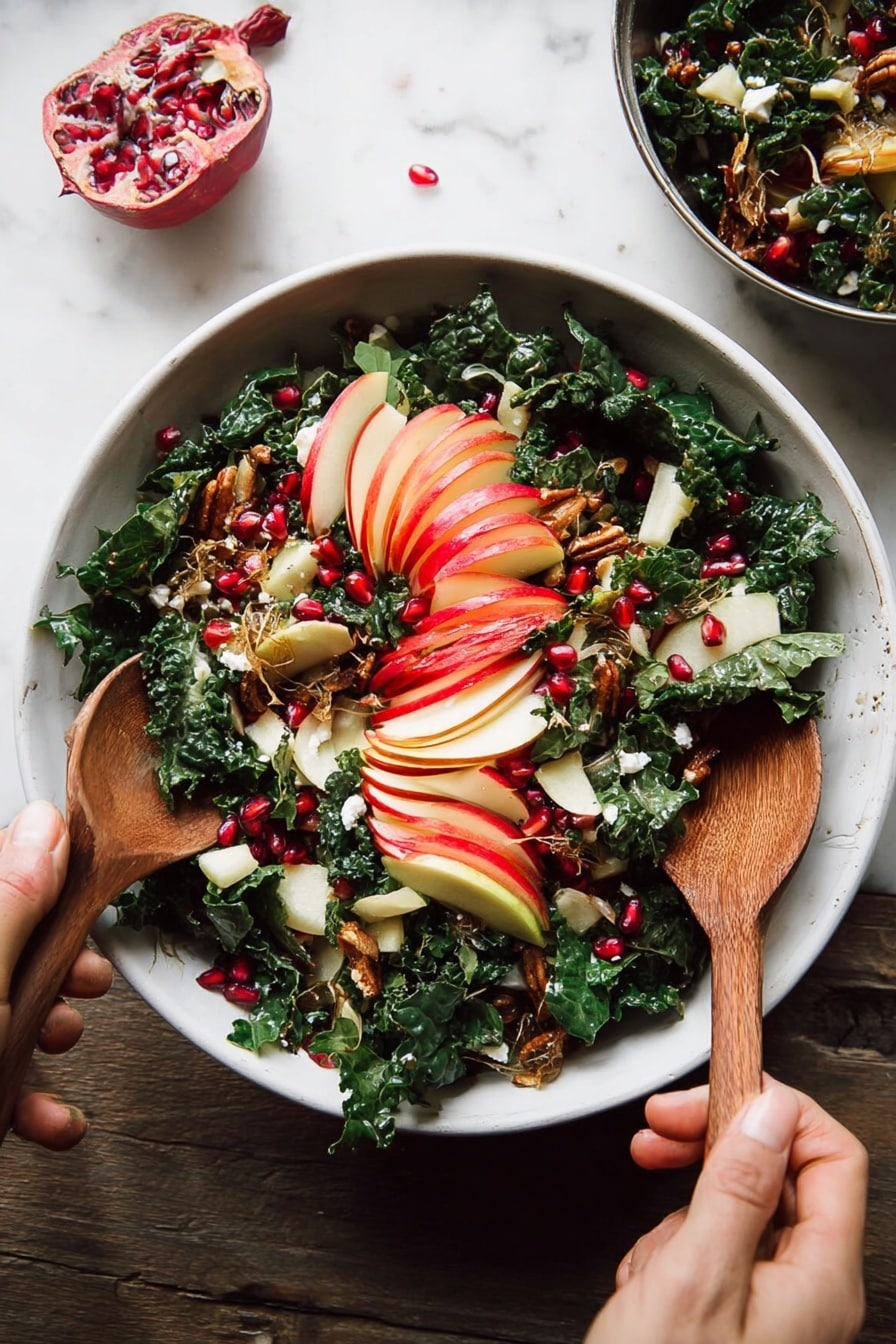 A white bowl filled with a fresh salad rests on a white marbled surface, showing layers of dark green chopped kale mixed with thin slices of red-skinned apple arranged in a fan shape on top. Bright red pomegranate seeds are scattered across the salad, adding spots of vibrant color. Golden brown toasted seeds and small bits of crispy brown topping are sprinkled on the salad for texture. Pieces of white cheese with a soft texture are visible beneath the kale. A woman's hand holds a wooden spoon on the bottom left while another woman's hand grips a second wooden spoon on the top right as they mix the salad. Photo taken with an iphone --ar 2:3 --v 7 - Fall Harvest Honeycrisp Apple and Kale Salad, autumn apple kale salad, healthy fall salads, Honeycrisp apple salad, kale salad with prosciutto