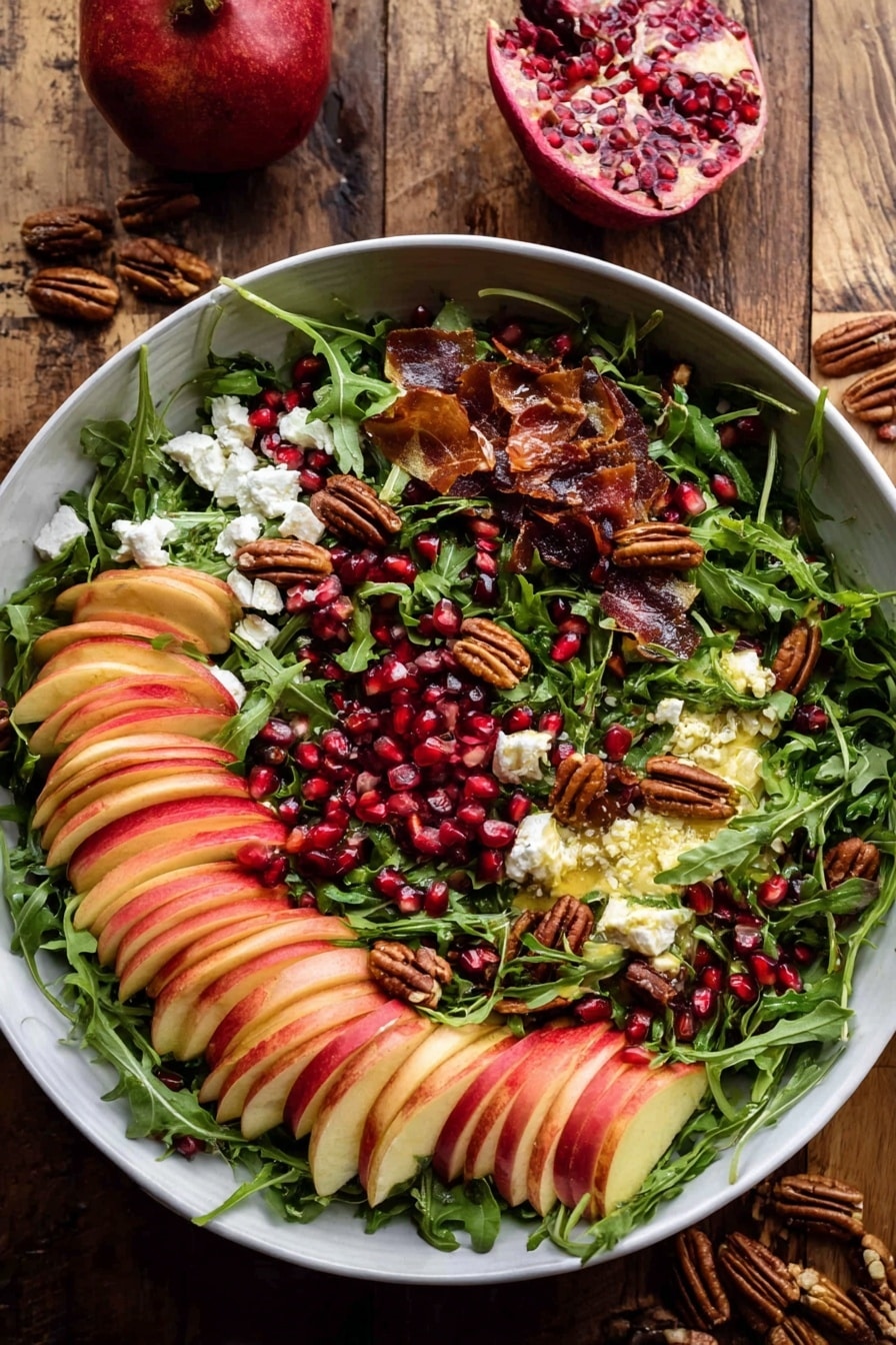 A large white bowl filled with a colorful salad resting on a wooden surface. The base layer is fresh green arugula leaves spread evenly, topped with neatly sliced red and light yellow apples arranged in fanned clusters scattered throughout. Small bits of white cheese are sprinkled over the salad, adding contrast. There are dark red pomegranate seeds dotted across the salad, mixed with toasted nuts that add a crunchy texture and deep brown color. Pieces of crispy, thin slices of brown bacon or prosciutto are interspersed, giving extra warmth to the colors. Two wooden salad spoons with smooth handles rest inside the bowl on opposite sides. In the background, half a pomegranate with bright red seeds is on a white plate, along with small bunches of fresh green herbs and a few stray nuts. The whole scene is against a white marbled texture. photo taken with an iphone --ar 2:3 --v 7 - Autumn Harvest Honeycrisp Apple and Feta Salad, fall fruit salad, autumn side dishes, honeycrisp apple salad, seasonal fall recipes