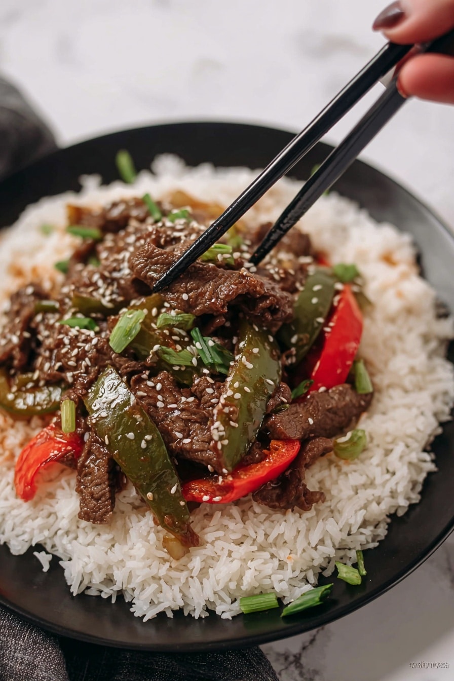 A white plate holds a large base layer of fluffy, long-grain white rice, spread evenly across the plate. On top of the rice sits a colorful stir-fry with three distinct elements: dark brown thin strips of cooked beef, glossy green bell pepper slices, and bright red bell pepper slices. The stir-fry is sprinkled with small white sesame seeds and chopped green onion pieces for freshness. Two black chopsticks rest across the top edge of the plate. The background shows a red bell pepper and green leafy herbs on a white marbled surface. Photo taken with an iphone --ar 2:3 --v 7 - Crockpot Pepper Steak, slow cooker beef dinner, easy crockpot recipes, hearty beef and bell peppers, comfort food slow cooker
