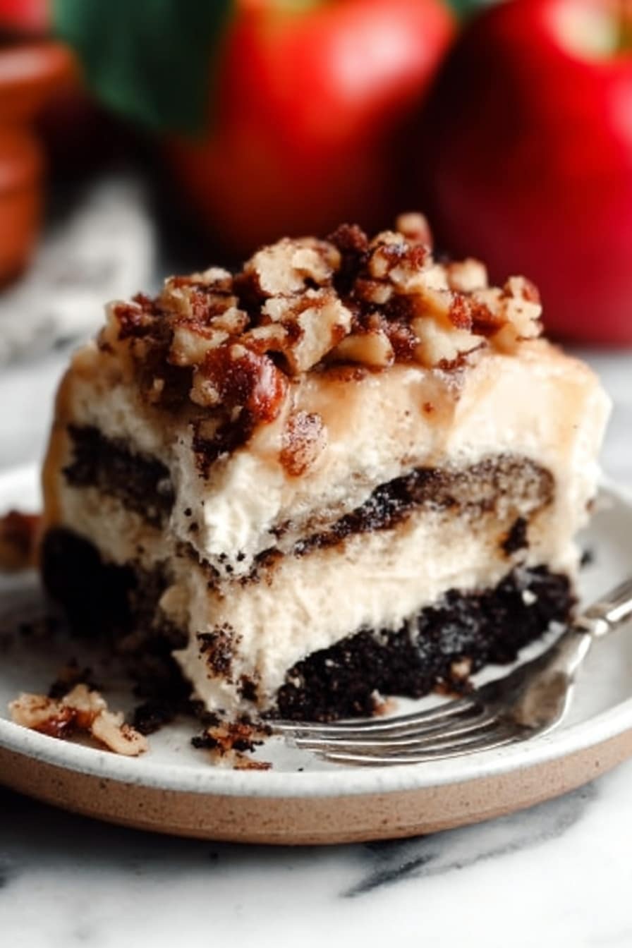 The image shows a close-up of a thick slice of layered dessert on a white plate. The bottom layer is dark and crumbly, looking like crushed chocolate cookies. Above that, there is a creamy, light beige layer that looks soft and smooth. On top, there is a sprinkle of chopped nuts mixed with small crumb pieces, giving a crunchy texture. A metal fork rests on the plate near the dessert. The background has a white marbled surface, and there are whole red apples blurred in the background. Photo taken with an iphone --ar 2:3 --v 7 - Apple Pie Cinnamon Rolls with Apple Cider Caramel Sauce and Cream Cheese Frosting, fall breakfast cinnamon rolls, apple cinnamon roll recipe, caramel apple cinnamon rolls, homemade apple cinnamon rolls