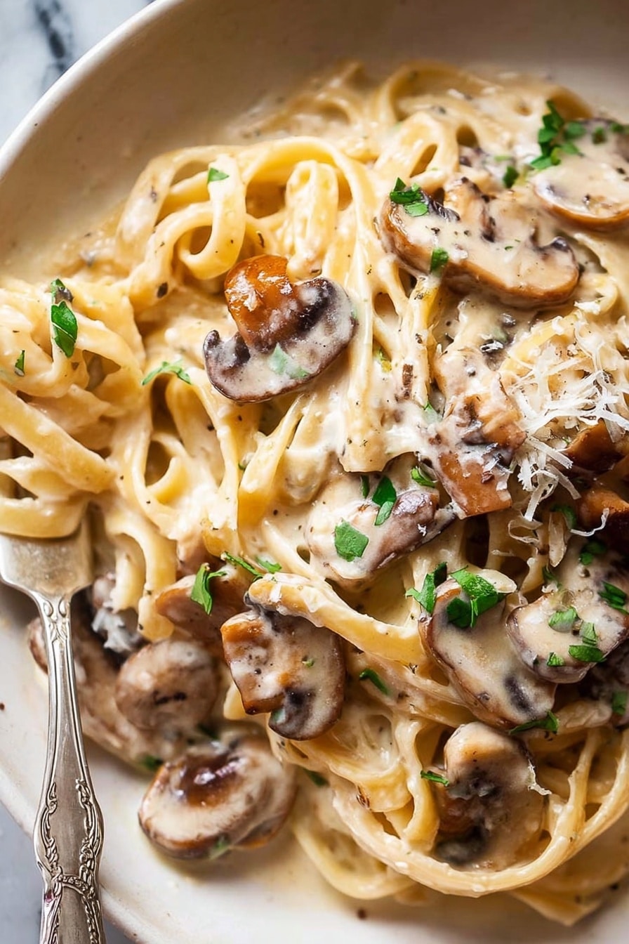 A close-up of creamy pasta with several long, flat noodles twisted and layered, covered in a smooth, off-white sauce. On top and mixed into the pasta are many thin slices of cooked mushrooms with a light brown color and soft texture. Small pieces of fresh green herbs are scattered over the whole dish, adding a splash of color. The dish is on a white plate with a fork partially wrapped in the pasta at the bottom left corner. The background is a white marbled texture. Photo taken with an iphone --ar 2:3 --v 7 - Creamy Mushroom Pasta, Mushroom Pasta Recipe, Easy Mushroom Pasta, Vegetarian Mushroom Pasta, Comfort Food Pasta