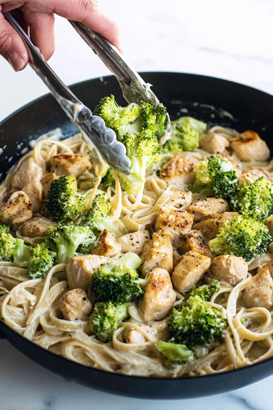 A close-up view of a black pan filled with creamy pasta layered at the bottom in a pale beige color with smooth texture. On top, there are chunks of cooked chicken pieces, golden brown with light black pepper spots, scattered evenly. Bright green broccoli florets, fresh and slightly steamed, are spread over the chicken and pasta. A woman's hand holding silver tongs with white sauce spots is seen in the upper right, picking up some broccoli and chicken. The background is a white marbled texture. photo taken with an iphone --ar 2:3 --v 7 - Creamy Chicken Broccoli Fettuccine Alfredo, Chicken Fettuccine Alfredo, Easy Chicken Pasta, Homemade Alfredo Sauce, Quick Weeknight Dinner