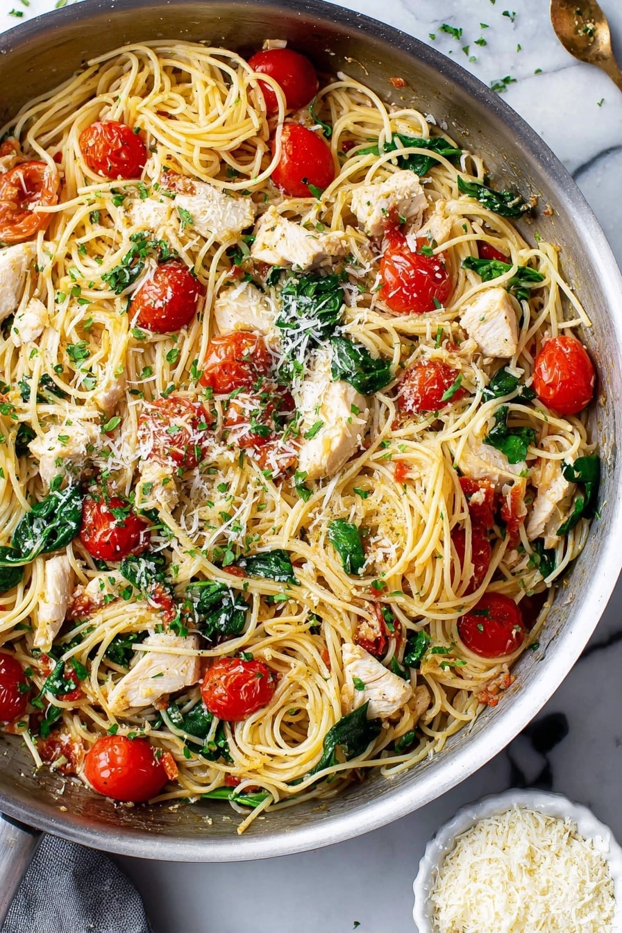 This image shows a pan filled with cooked thin spaghetti mixed with white chicken pieces, bright red cherry tomatoes cut in halves, and fresh green spinach leaves scattered throughout. The pasta looks soft and tangled, and there are small sprinkles of grated cheese and finely chopped green herbs on top. The pan sits on a white marbled surface, and near the bottom right corner, there is a small white bowl filled with more grated cheese. The whole dish looks fresh and colorful. photo taken with an iphone --ar 2:3 --v 7 - Easy Chicken Scampi with Cherry Tomatoes and Spinach, chicken scampi recipe, quick chicken dinner, healthy chicken pasta, lemon garlic chicken