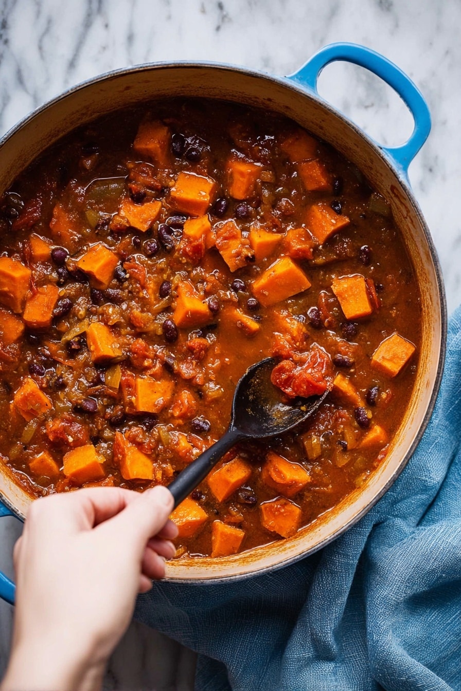 A large blue pot filled with a thick rich stew that has many small orange cubes of sweet potato, dark beans, and pieces of tomato in a brownish-red liquid. The stew has visible chunks of onion and a textured look from the cooked ingredients. A woman's hand is holding a black spoon, stirring the stew gently. The pot is placed on a white marbled surface, with a soft blue cloth nearby. Photo taken with an iphone --ar 2:3 --v 7 - Sweet Potato Black Bean Soup, healthy vegan soup, easy vegetarian dinner, hearty fall soup, plant-based comfort food