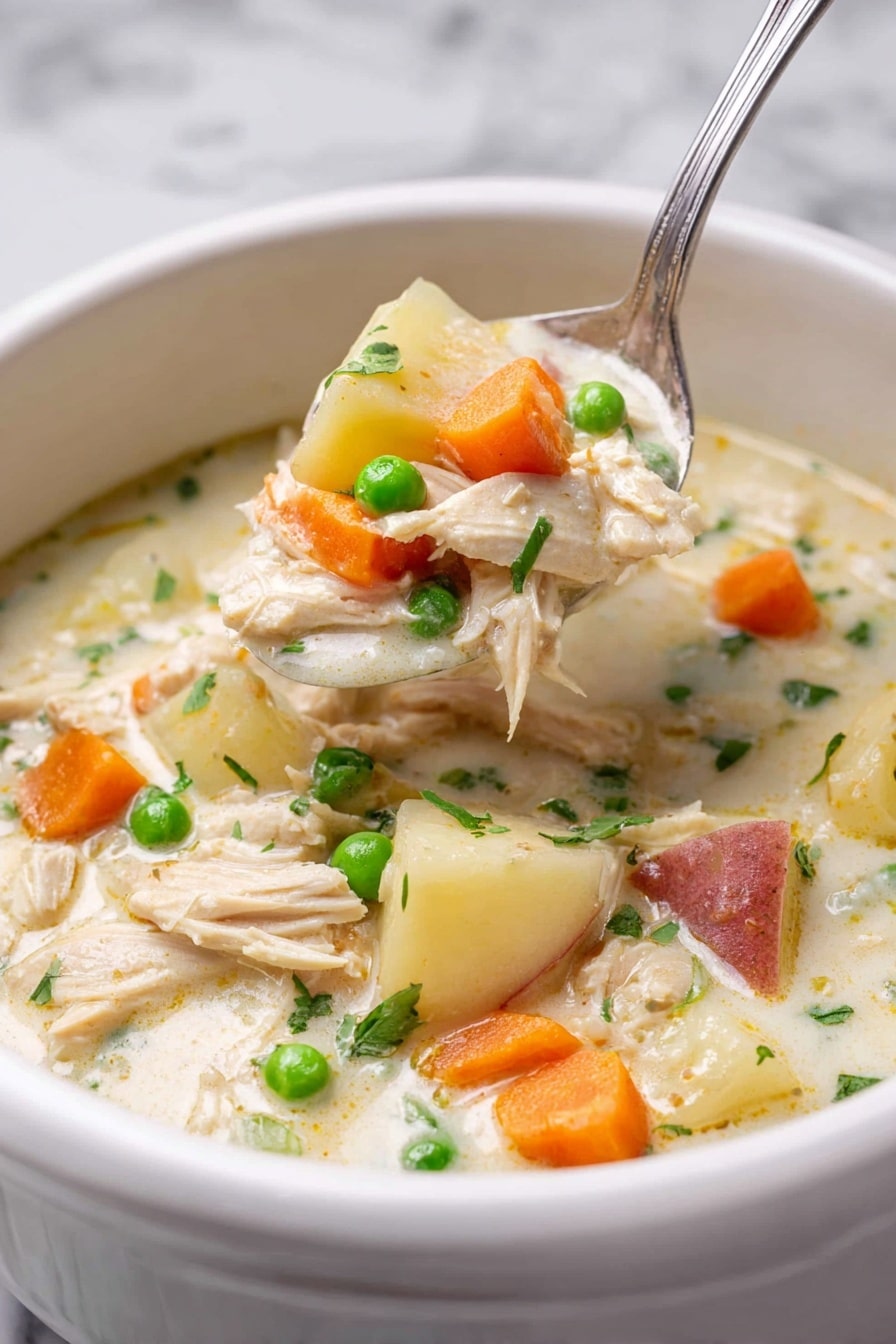 A white bowl filled with thick creamy chicken soup shows several layers: the base is a light cream broth, with chunks of light beige shredded chicken, bright orange carrot slices, small green peas, and white potato pieces with reddish skin. A silver spoon lifts a scoop of the soup, filled with all these colorful ingredients, positioned slightly above the bowl. The background is a white marbled texture, giving a clean and fresh look to the image. Photo taken with an iphone --ar 2:3 --v 7 - Slow Cooker Garlic Parmesan Chicken Stew, easy chicken stew recipes, creamy garlic chicken, hearty slow cooker meals, comforting chicken stew
