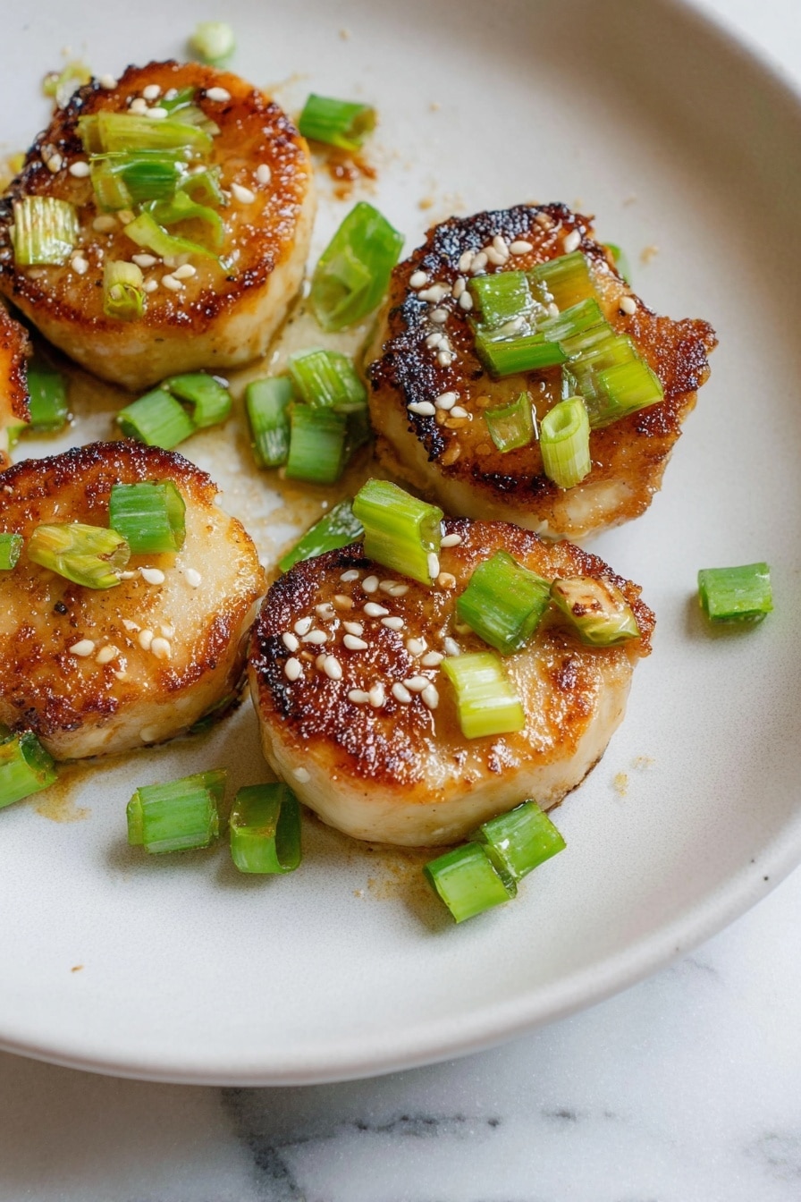 The image shows five small round pieces of golden-brown cooked food with a slightly crispy and caramelized texture on top. Each piece is garnished with small green chopped scallions and sprinkled with white sesame seeds. They are arranged on a white plate with a smooth, slightly matte surface, placed on a white marbled textured background. The food looks warm and freshly cooked, with the colors of golden brown, light green, and white creating a fresh and appetizing look. photo taken with an iphone --ar 2:3 --v 7 - Miso Soy King Oyster Mushroom, vegan scallops, vegan seafood alternative, mushroom recipes, plant-based seafood