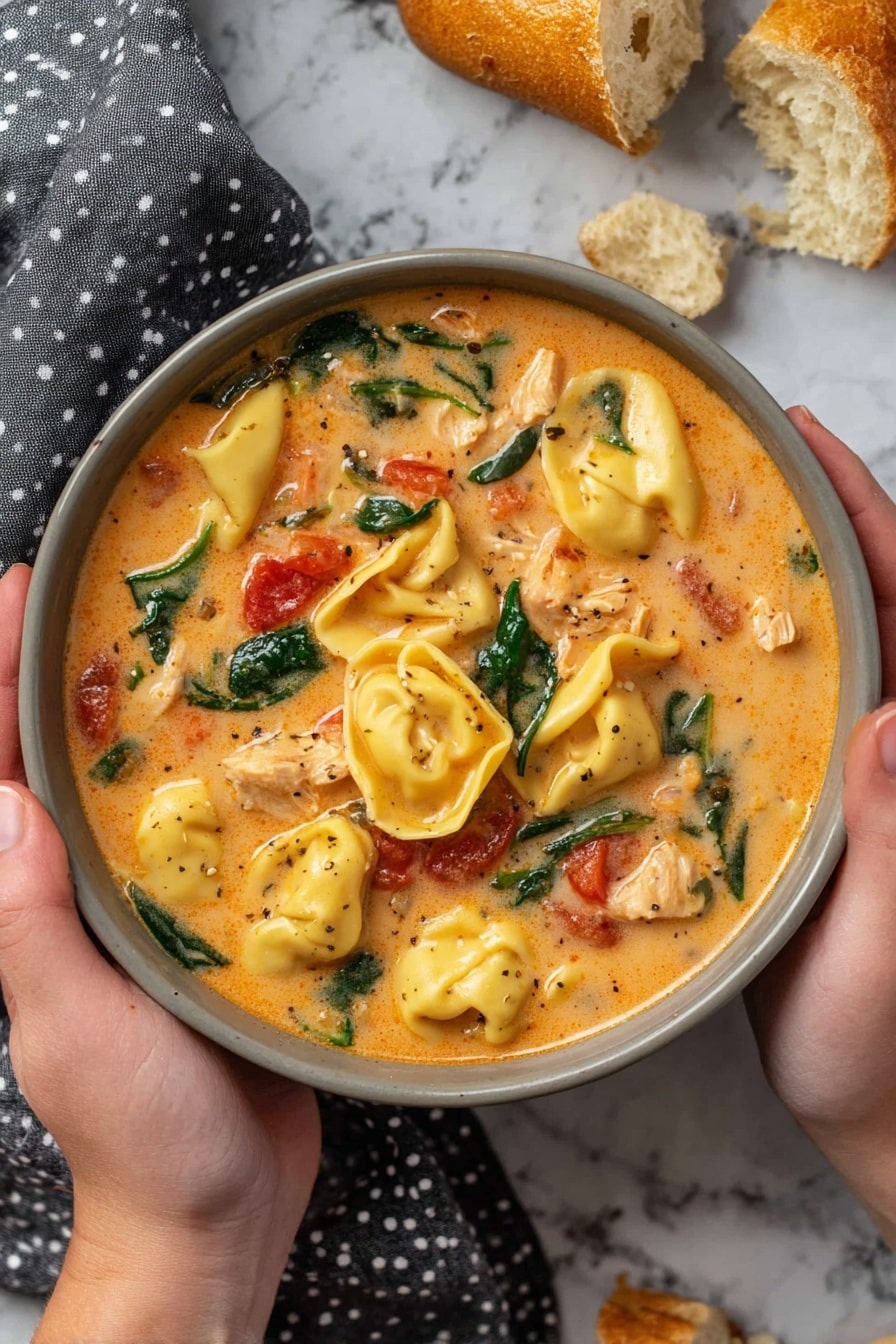 A black slow cooker filled with creamy orange soup containing plump yellow tortellini pasta, scattered fresh dark green spinach leaves, and small red tomato pieces mixed in a smooth sauce with visible bits of white shredded chicken, a curved wooden spoon resting inside the cooker, placed on a white marbled surface with pieces of toasted bread on a gray cloth nearby photo taken with an iphone --ar 2:3 --v 7 - Creamy Chicken Tortellini Soup Crock Pot, easy slow cooker tortellini soup, comforting chicken tortellini dinner, cheesy tortellini soup recipe, hearty chicken pasta soup