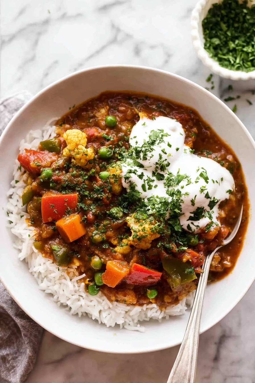 A white bowl filled with a base layer of white rice topped with a colorful vegetable curry. The curry has pieces of orange carrots, bright green peas, red bell peppers, and bits of cauliflower all mixed in a rich reddish-brown sauce. On top of the curry, there are two dollops of smooth white yogurt sprinkled with chopped green herbs. A silver spoon rests inside the bowl on the right side. The bowl is placed on a white marbled surface, and in the background, there is a small white bowl filled with chopped green herbs. photo taken with an iphone --ar 2:3 --v 7 - Vegetable Curry, healthy vegetable curry recipe, easy vegetable curry, hearty vegan curry, spicy vegetable curry