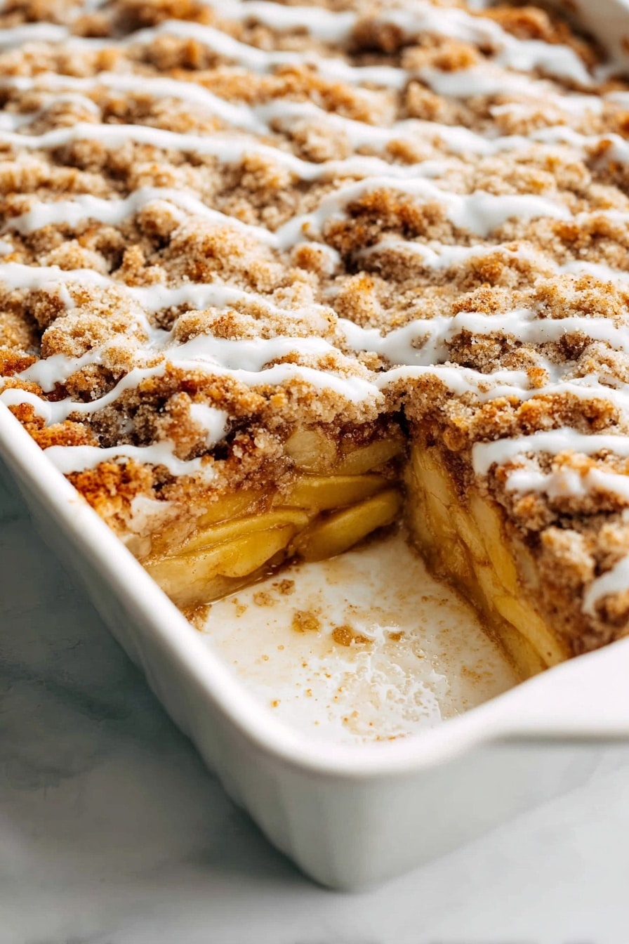 A white baking dish holds a multi-layered baked dessert with three visible layers. The bottom layer is made of soft cooked apple slices, pale yellow in color, resting on a thin, golden crust. Above this, there is a thick, light brown crumbly streusel layer that looks crunchy and uneven, covering the apples. A thin, slightly shiny drizzle of white icing runs lightly across the top streusel layer in wavy lines. The edges of the dish show some baked-on residue, adding a homemade feel. The white marbled surface beneath the dish adds a clean, bright background. photo taken with an iphone --ar 2:3 --v 7 - Apple French Toast Casserole, Apple French Toast Bake, Easy Apple Breakfast, Cinnamon Apple Brunch, Make-Ahead Breakfast Casserole