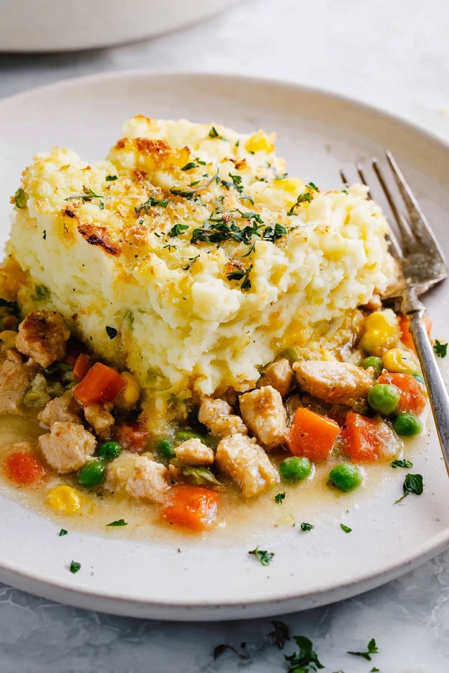 The dish shows two layers on a white plate with a white marbled surface below. The bottom layer is a mix of small pieces of light brown cooked chicken, bright orange carrot cubes, green peas, and some yellow bits, all in a light sauce. The top layer is a thick, fluffy heap of mashed potatoes with a pale yellow color and a slightly browned, baked texture on the edges. Small green herb pieces are sprinkled over the top and around the plate. A metal fork rests on the right side of the plate. photo taken with an iphone --ar 2:3 --v 7 - Healthy Turkey Shepherd's Pie, healthy shepherd's pie recipe, turkey casserole with veggies, low-fat comfort food, nutritious shepherd's pie