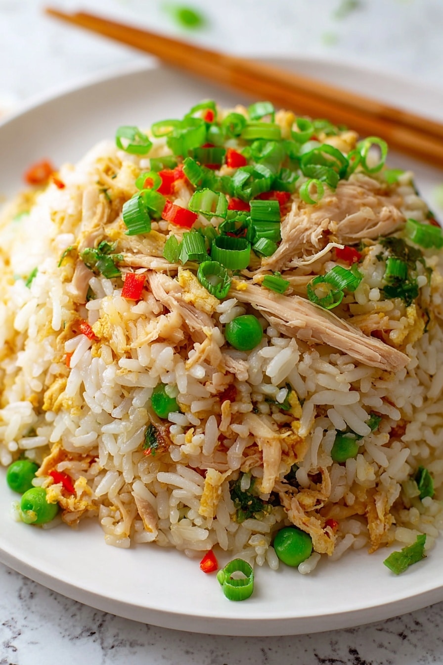 A close-up view of a mound of fried rice on a white plate, placed on a white marbled surface. The dish has three main layers: the bottom layer is white and slightly golden rice grains, the middle layer contains shredded light brown chicken pieces mixed with small green peas, and the top layer is scattered with bright green chopped spring onions and tiny red bell pepper bits. Wooden chopsticks rest diagonally at the back of the plate. Photo taken with an iphone --ar 2:3 --v 7 - Easy Chicken Fried Rice, quick chicken fried rice, easy fried rice recipe, homemade chicken fried rice, best chicken fried rice