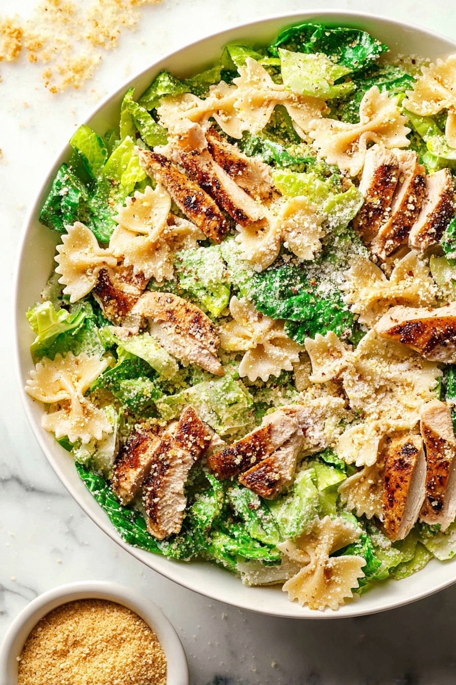 A large white bowl filled with a colorful salad showing layers of light green leafy lettuce pieces mixed with beige farfalle pasta shapes. On top of this are slices of browned, cooked chicken that have a slightly crispy texture. The dish is sprinkled with light brown grated cheese and breadcrumbs, giving a crumbly look over the salad. The bright green lettuce pieces and the pasta form the base layer, with chicken pieces scattered evenly above. The white marbled surface underneath adds a clean look, and there is a small bowl of extra breadcrumbs on the side. photo taken with an iphone --ar 2:3 --v 7 - Chicken Caesar Pasta Salad, Chicken Caesar Pasta, Caesar Pasta Salad, Easy Chicken Pasta Salad, Make-Ahead Pasta Salad