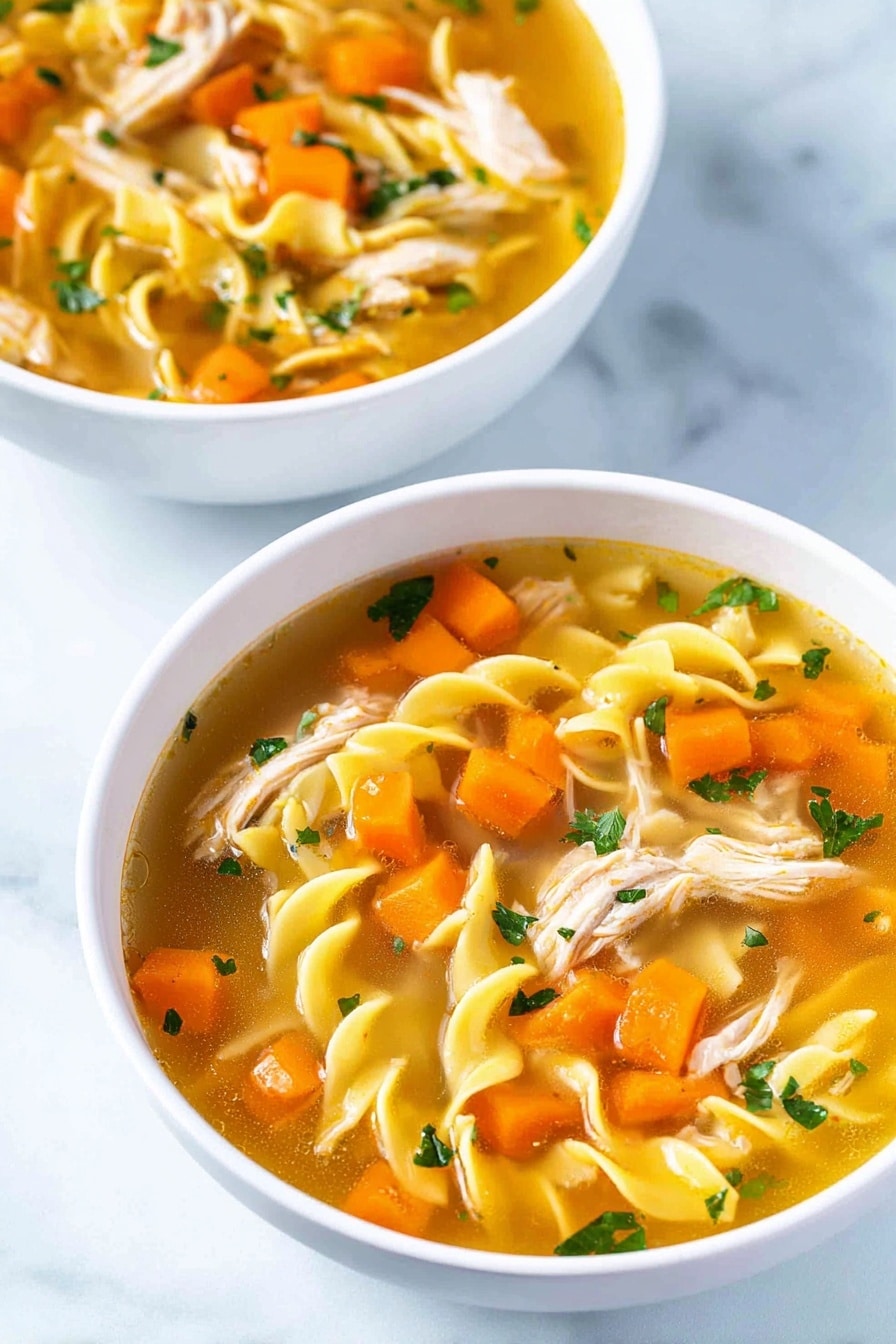 Two white bowls sit on a white marbled surface, each filled with a clear golden broth soup. Inside the soup are three main layers: bright orange carrot cubes scattered throughout, shredded pale pink chicken pieces, and yellow twisted egg noodles floating, mixed with small chopped green herbs and translucent onion bits. The colors mix well, creating a warm and fresh look. photo taken with an iphone --ar 2:3 --v 7 - Homemade Chicken Noodle Soup, comforting chicken noodle soup, homemade chicken soup recipe, easy chicken noodle soup, flavorful chicken soup