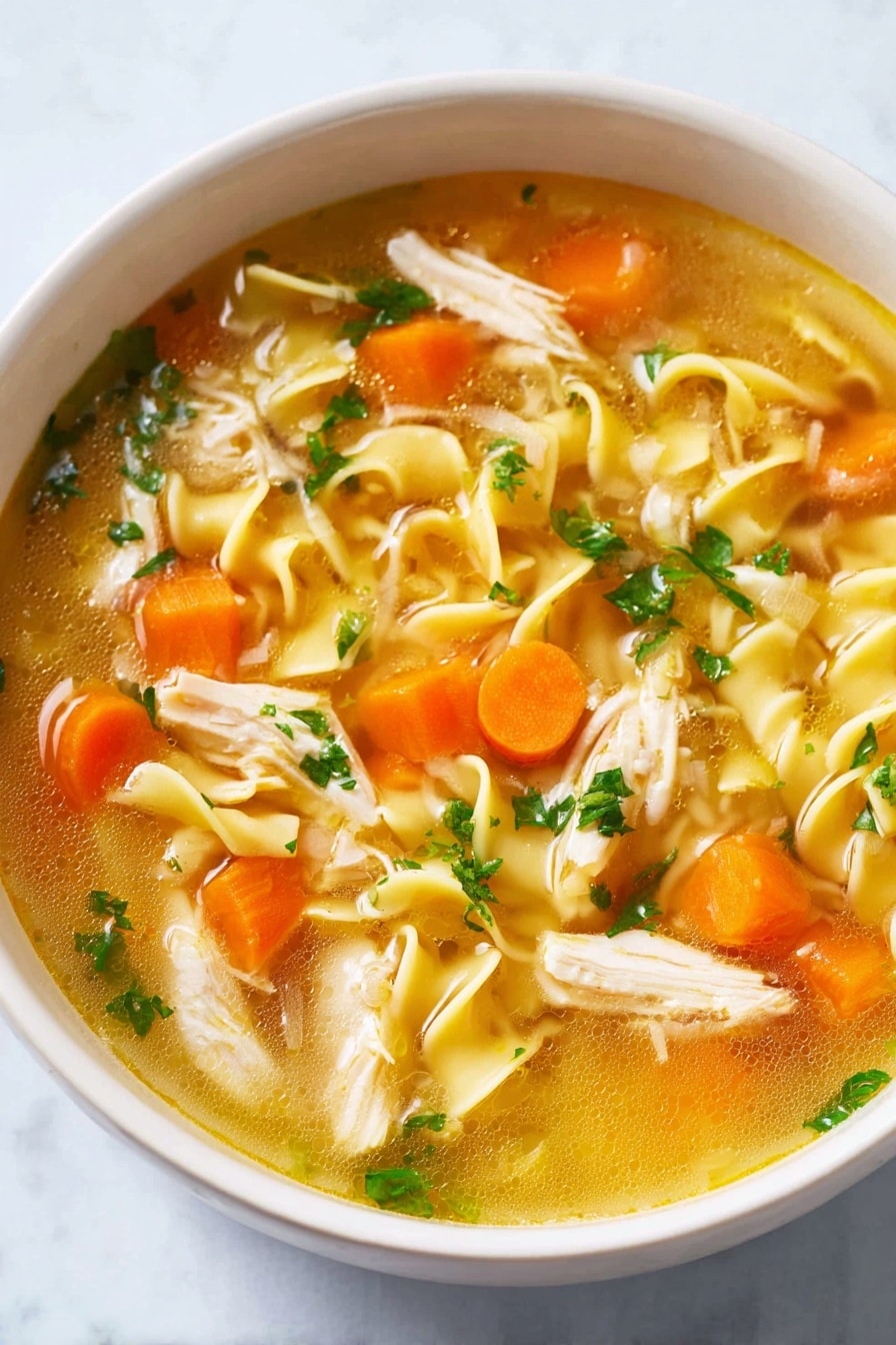 A white bowl filled with clear golden broth containing curly yellow noodles, bright orange carrot cubes, soft white onion pieces, light beige shredded chicken, and small green parsley leaves scattered on top, all resting on a white marbled surface photo taken with an iphone --ar 2:3 --v 7 - Homemade Chicken Noodle Soup, comforting chicken noodle soup, homemade chicken soup recipe, easy chicken noodle soup, flavorful chicken soup