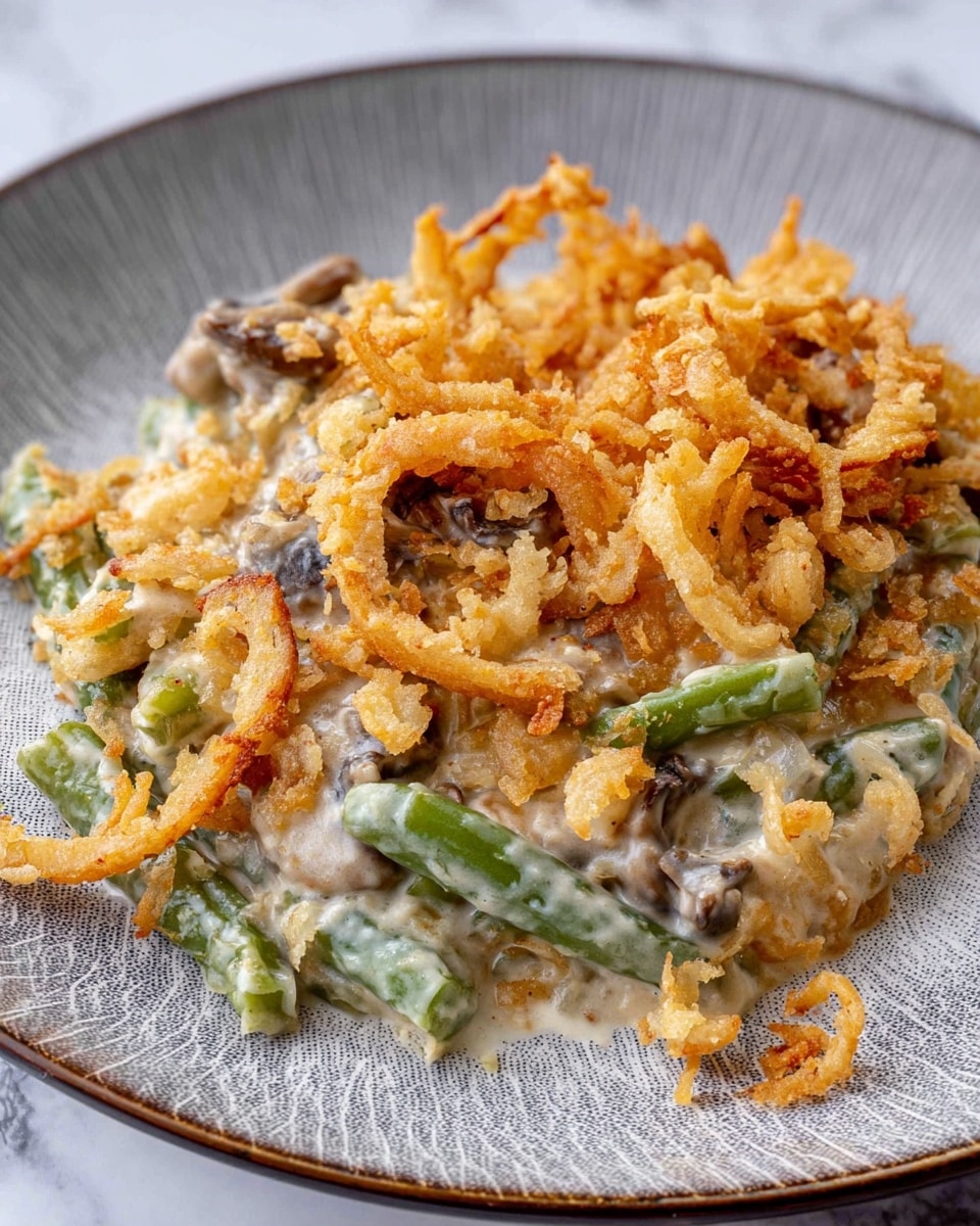 A serving of creamy green bean casserole on a white plate with a gray textured pattern. The dish has soft green beans mixed into a thick white creamy sauce with small chunks of mushrooms visible. The top layer is covered with golden-brown crispy fried onion rings and smaller fried onion pieces scattered unevenly. The casserole’s texture shows both creamy smoothness and crunchy fried bits, with the green beans peeking through. The background is a white marbled surface. photo taken with an iphone --ar 4:5 --v 7
