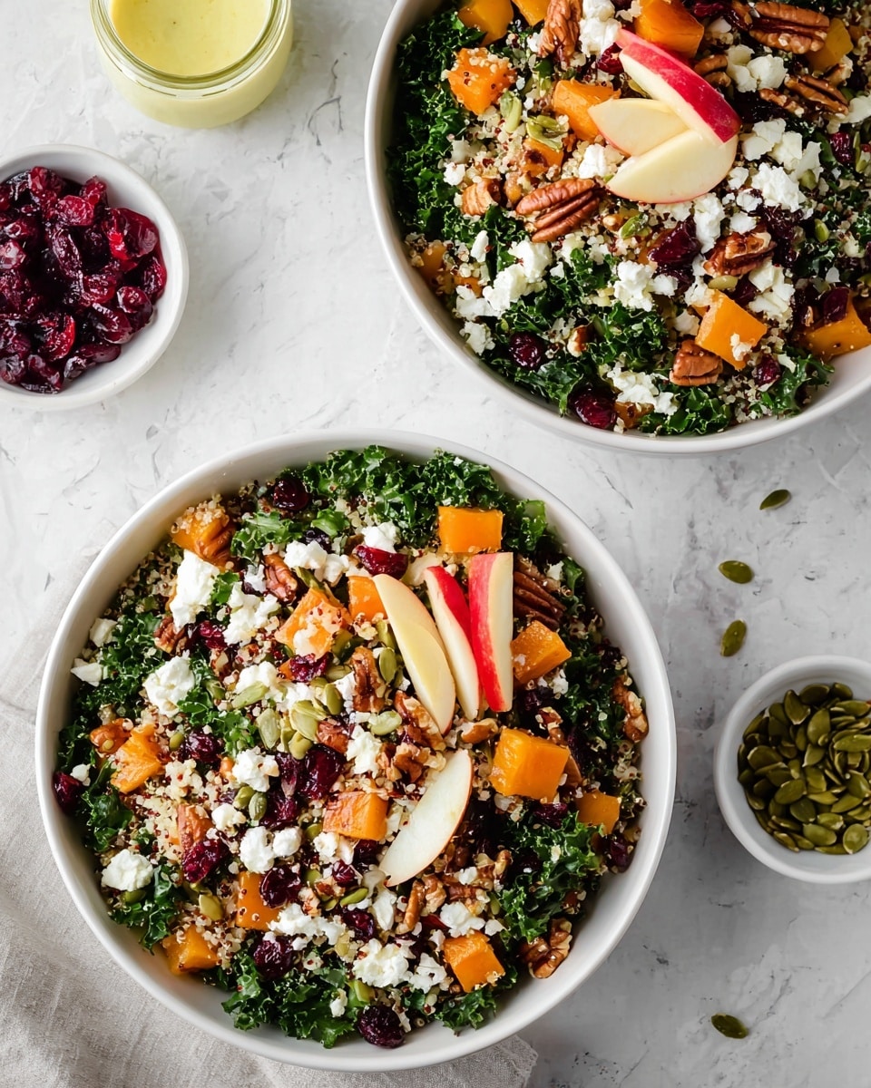 A white bowl holds a fresh salad with multiple layers: the base is made of dark green curly kale leaves, mixed evenly with small light beige quinoa grains. On top, bright orange chunks of soft squash or pumpkin are scattered throughout. Thin red and white slices of apple add a crisp texture and color contrast, placed randomly among the greens. Small, dark red dried cranberries are mixed in, providing pops of deep color. There are also light brown pecan halves and green pumpkin seeds spread across the salad, along with small white crumbles of cheese that contrast with the other colors. The bowl sits on a white marbled surface, and the photo is taken with an iphone --ar 4:5 --v 7