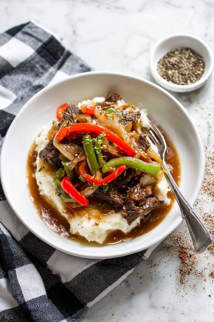 A white shallow bowl holds a layered dish with mashed potatoes at the bottom, creamy white and soft in texture. On top, there are strips of beef cooked dark brown, mixed with sautéed red and green bell pepper slices, and translucent cooked onions. The layers are covered with a glossy brown gravy that pools slightly at the base. A silver fork rests on the edge of the bowl. The bowl sits on a black and white checkered cloth, placed on a white marbled surface. To the top right, there is a small white dish with cracked black pepper scattered around it. photo taken with an iphone --ar 2:3 --v 7 - Pepper Steak with Onion, Pepper Steak with Onion recipe, savory pepper steak, quick beef stir-fry, flavorful flank steak with peppers