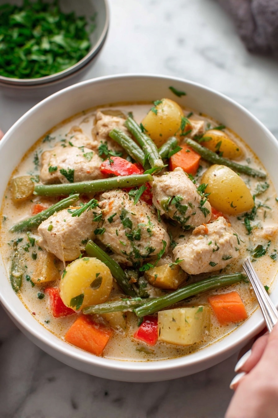 A white bowl filled with creamy chicken stew, showing large pieces of light brown chicken and chunky vegetables including orange carrots, green beans, yellow potatoes, and small bits of red pepper, all mixed in a thick, pale sauce with visible herbs on top; in the background, a bowl of chopped green herbs rests on a white marbled surface, and a woman's hand holding a spoon is partly visible at the bottom right. photo taken with an iphone --ar 2:3 --v 7 - Hearty Chicken and Root Vegetable Stew, Chicken and Root Vegetable Stew, Comfort Food Stew, Nourishing Chicken Stew Recipe, Cozy Root Vegetable Soup