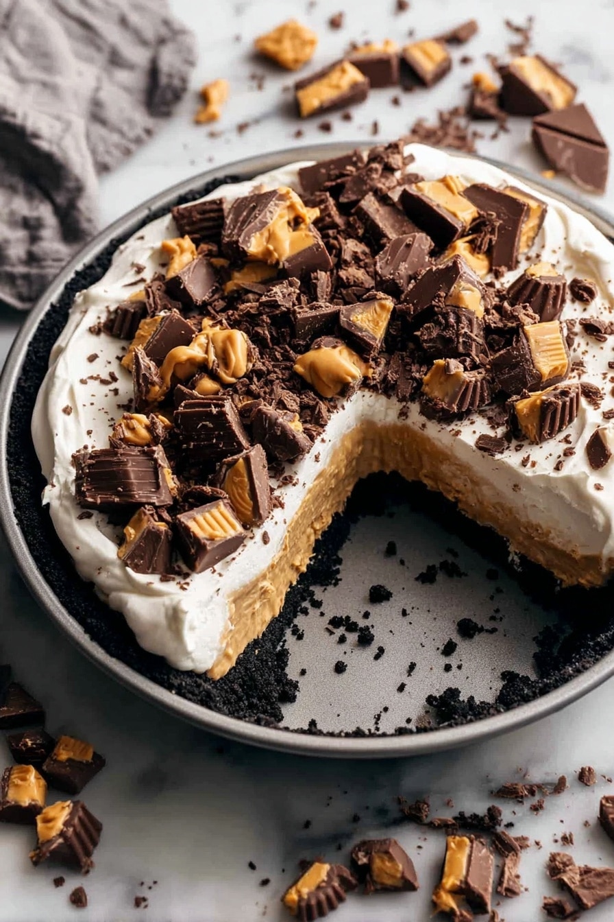 A round dessert in a gray pan has three layers: a dark crumbled base, a thick light brown peanut butter layer, and a smooth white cream layer on top. The cream is covered with many pieces of dark chocolate and peanut butter candy scattered unevenly. The pan is placed on a white marbled surface with more pieces of the same chocolate candy spread around it. A large wedge is missing from the dessert, showing the three colorful layers clearly. photo taken with an iphone --ar 2:3 --v 7 - Chocolate Peanut Butter Pie, easy peanut butter chocolate dessert, no-bake pie recipes, creamy peanut butter pie, decadent chocolate pie