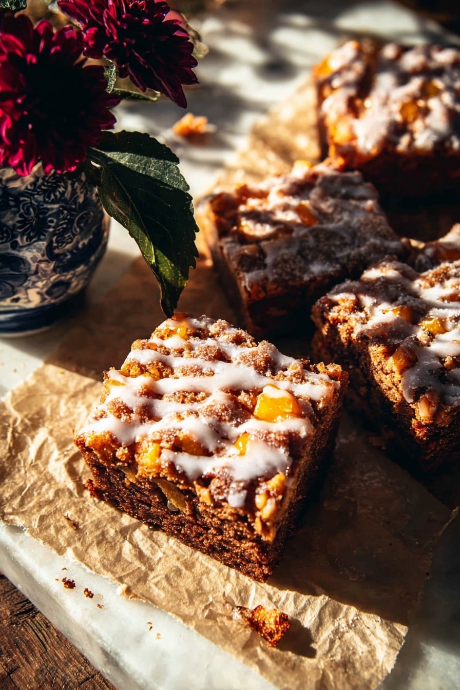 The image shows three thick square slices of a baked dessert with a dark brown base full of small orange chunks inside, topped with a light drizzle of white glaze that has a shiny and smooth texture. The dessert slices sit on crinkled parchment paper with some scattered crumbs around. To the top left, there is a small blue and white vase holding a dark red flower with deep green leaves. The whole scene is lit by warm sunlight creating strong shadows and highlights, placed on a white marbled surface photo taken with an iphone --ar 2:3 --v 7 - Glazed Honeycrisp Apple Fritter Cake, apple fritter dessert, fall apple cake, easy apple cake recipe, Honeycrisp apple recipes