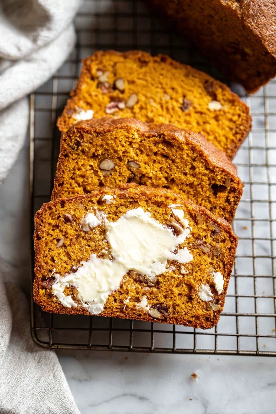 The image shows three thick slices of moist, orange-brown bread with small pieces of nuts inside, laid out on a metal cooling rack. The front slice is spread with melting white butter that contrasts with the bread’s warm color, showing a soft and slightly crumbly texture. The nuts inside the bread add darker brown spots throughout. The cooling rack is placed on a white marbled surface, and part of a white cloth is visible in the background. photo taken with an iphone --ar 2:3 --v 7 - Easy Pumpkin Bread, Pumpkin Bread Recipe, Moist Pumpkin Bread, Autumn Pumpkin Loaf, Quick Pumpkin Bread