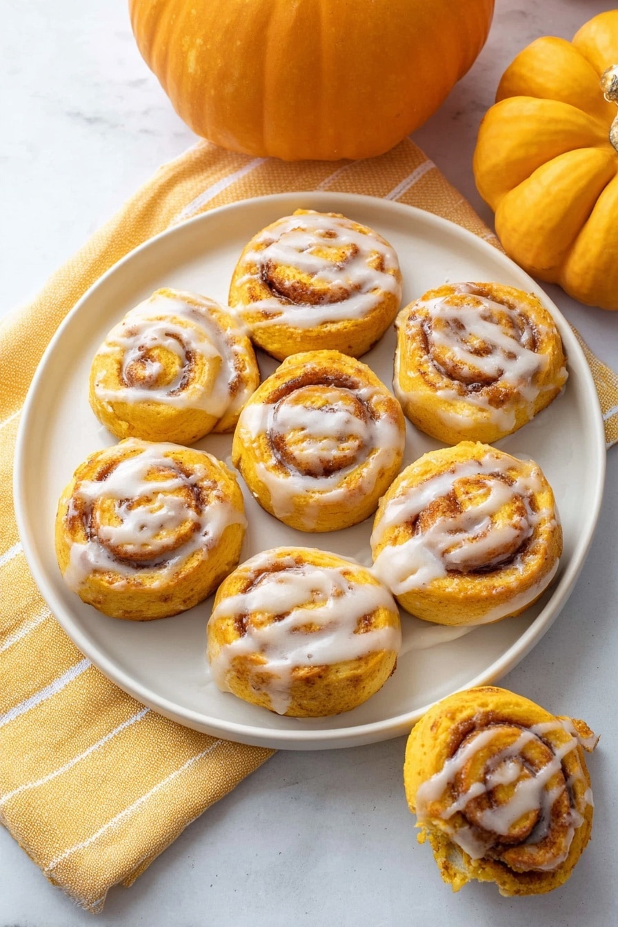 A round white plate holds nine small pumpkin-colored cinnamon rolls arranged in a loose circle. Each roll has light orange and brown swirls visible from the cinnamon filling and is topped with a thin drizzle of white icing, creating a shiny contrast. The plate sits on a soft yellow towel with a white line pattern, placed on a white marbled surface. Two whole pumpkins, one larger and one smaller, sit in the background, adding an autumn feel to the scene. One additional cinnamon roll is partially seen on the bottom right, held by a woman's hand, showing the flaky texture inside. Photo taken with an iphone --ar 2:3 --v 7 - Pumpkin Cinnamon Rolls, easy fall breakfast, no yeast cinnamon rolls, pumpkin dessert recipes, quick pumpkin sweet rolls