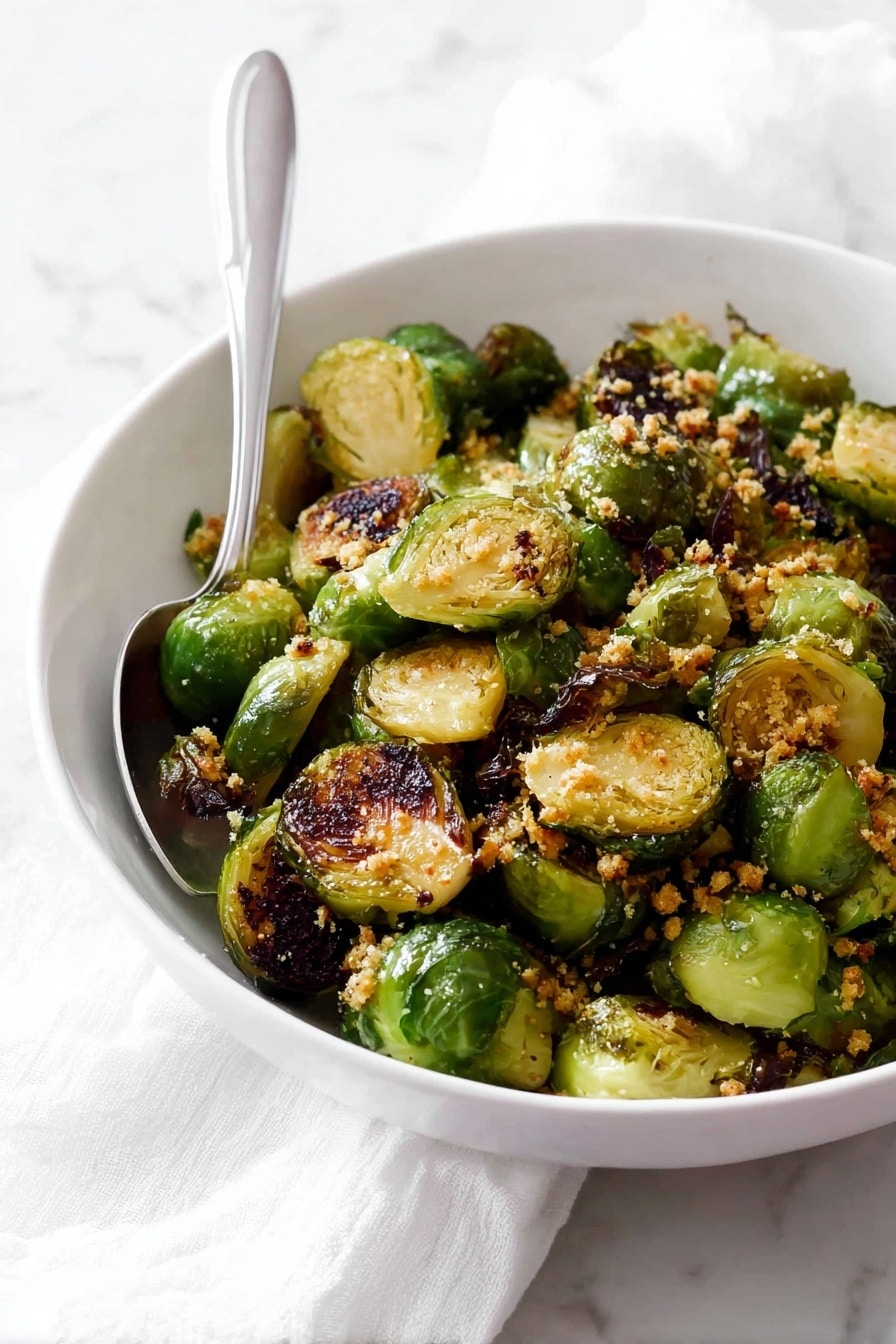 A white bowl filled with two layers of roasted Brussels sprouts, each piece halved to show a mix of light green interiors and crispy dark brown charred edges, giving a textured look; sprinkled with small bits of golden-brown garlic or breadcrumbs on top, a silver spoon placed inside the bowl rests against the side; the bowl is set on a white marbled surface with a white cloth nearby, creating a simple, clean setting. photo taken with an iphone --ar 2:3 --v 7 - Garlic Butter Brussels Sprouts, Brussels Sprouts with Garlic and Butter, Easy Roasted Brussels Sprouts, Healthy Brussels Sprouts Side Dish, flavorful Brussels Sprouts Recipe