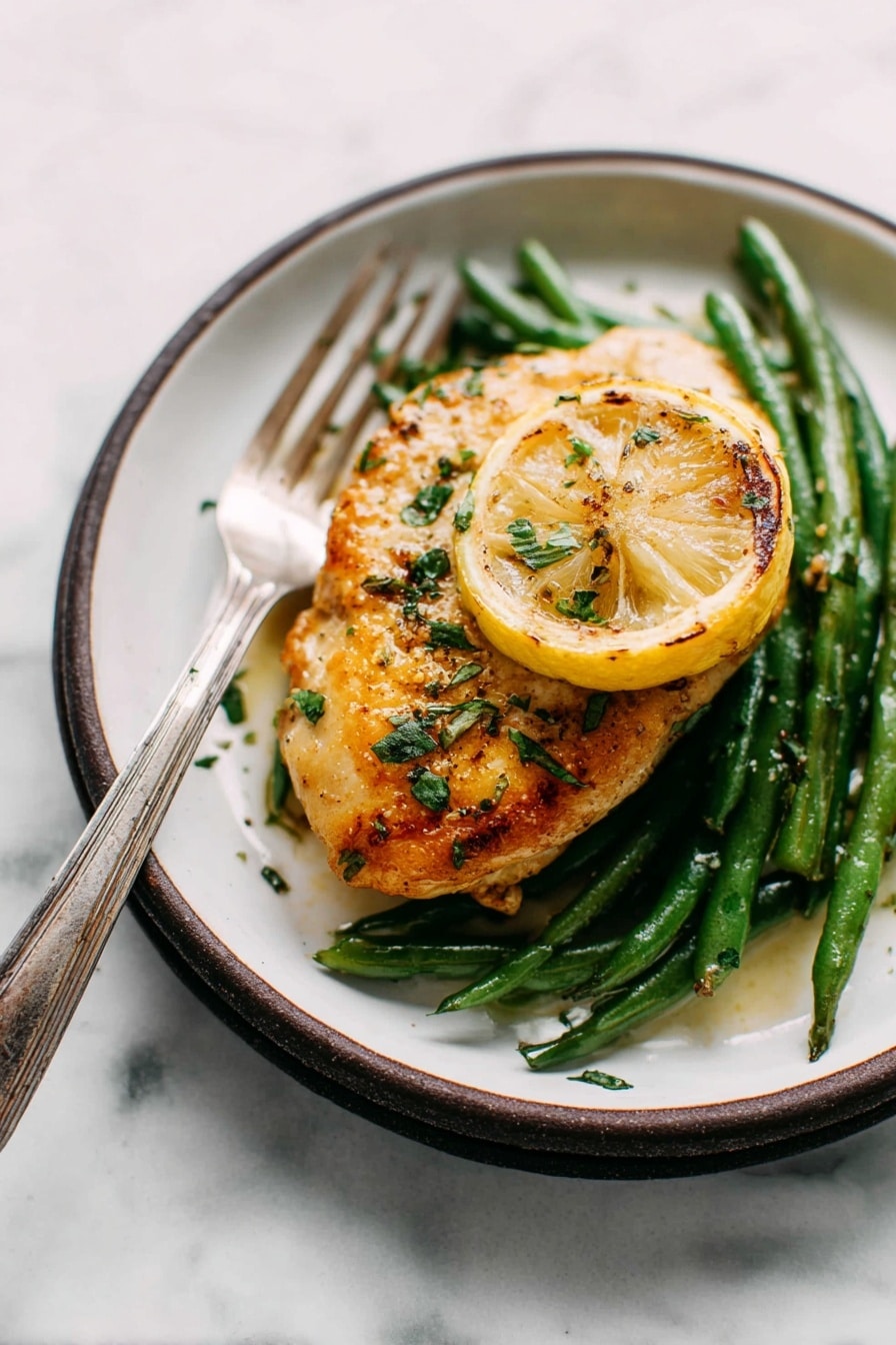 The image shows a single piece of golden-brown cooked chicken placed on top of a bed of green beans. Under the chicken, there is a slice of grilled lemon adding a pop of yellow color. The chicken is sprinkled with fresh green herbs and some seasoning that gives it a slightly glossy texture. The dish is served on a white plate with a dark rim, and a silver fork with an aged handle is resting on the edge of the plate. The surface beneath the plate has a white marbled texture, creating a clean and simple background. photo taken with an iphone --ar 2:3 --v 7 - Garlic Lemon Butter Chicken Skillet, easy chicken skillet recipes, quick chicken dinner, flavorful chicken recipes, weeknight chicken ideas