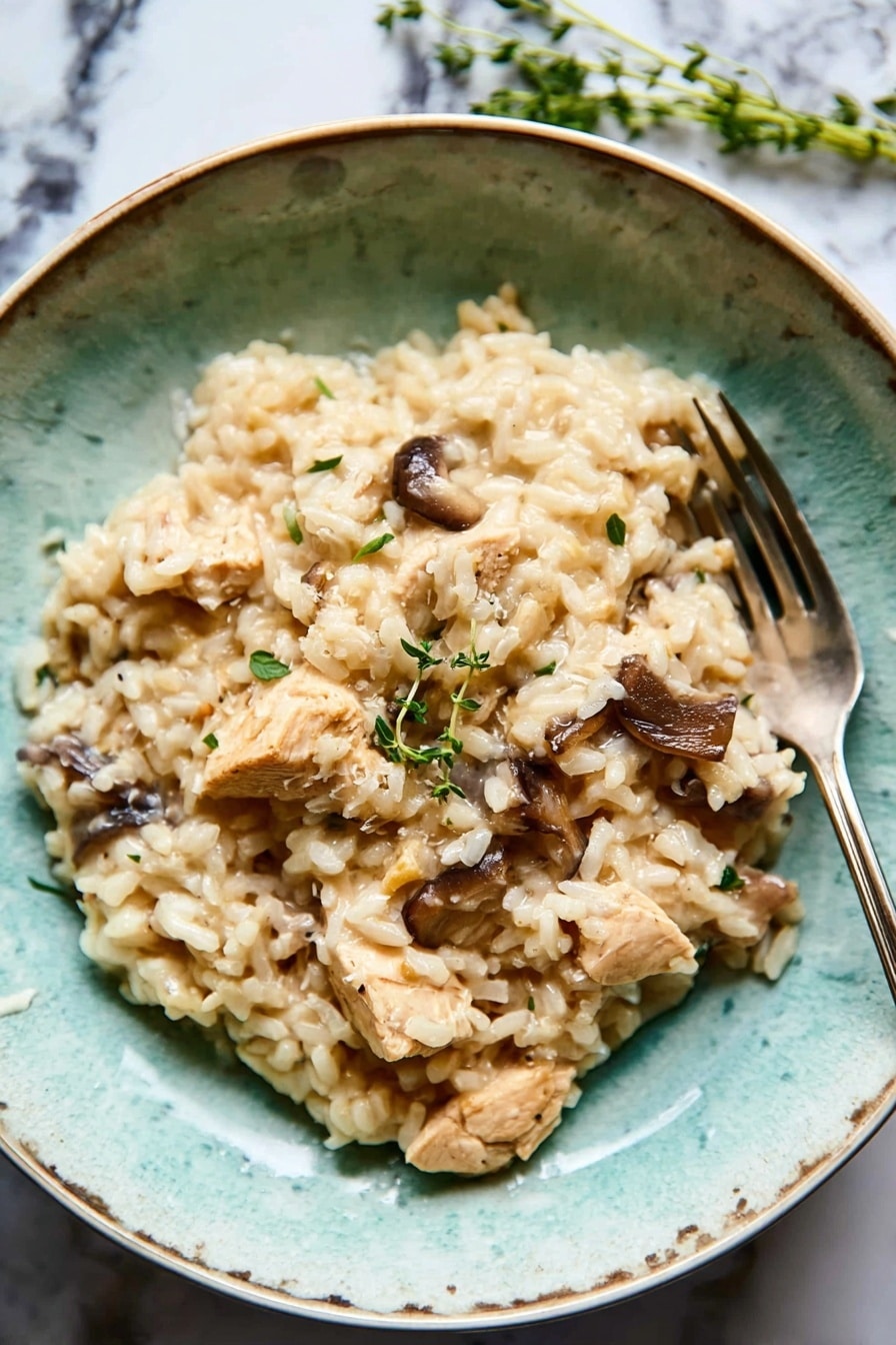 A textured turquoise bowl filled with creamy light beige risotto as the base layer, mixed with medium brown whole mushrooms and light tan chunks of chicken scattered evenly on top. A few sprigs of fresh green herbs sit on one side, adding a pop of color. The bowl rests on a white marbled surface with a folded dark grey cloth nearby, and a silver fork placed inside the bowl on the right side. The overall look is soft and earthy, with natural lighting enhancing the creamy texture of the dish photo taken with an iphone --ar 2:3 --v 7 - Chicken Mushroom Risotto with Thyme, Chicken Mushroom Risotto, Creamy Mushroom Risotto, Easy Chicken Risotto, Thyme Infused Risotto