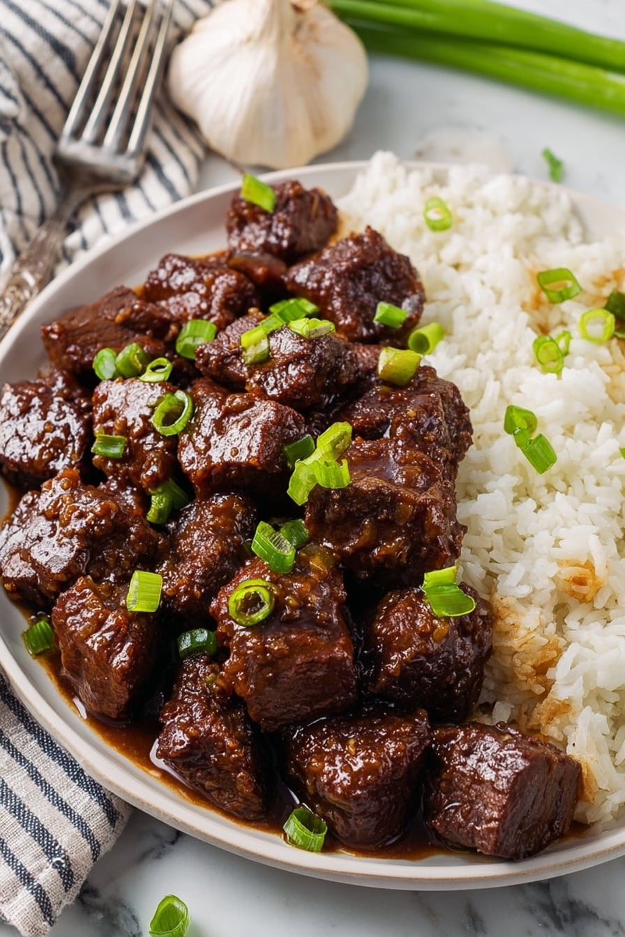 The image shows a white plate filled with two main layers: on the left and center, there are glossy, dark brown cubes of beef coated in a thick sauce, with chopped green onions sprinkled over the top, and on the right side, there is a layer of white rice with some sauce seeping into it. The plate is placed on a white marbled surface with a garlic bulb, a striped cloth, and a fork nearby. The focus is close, highlighting the texture of the tender beef and the fresh green garnish. Photo taken with an iphone --ar 2:3 --v 7 - Honey Garlic Steak Bites, Honey Garlic Steak Bites recipe, Easy Steak Bites, Quick Dinner Ideas, Delicious Steak Bites