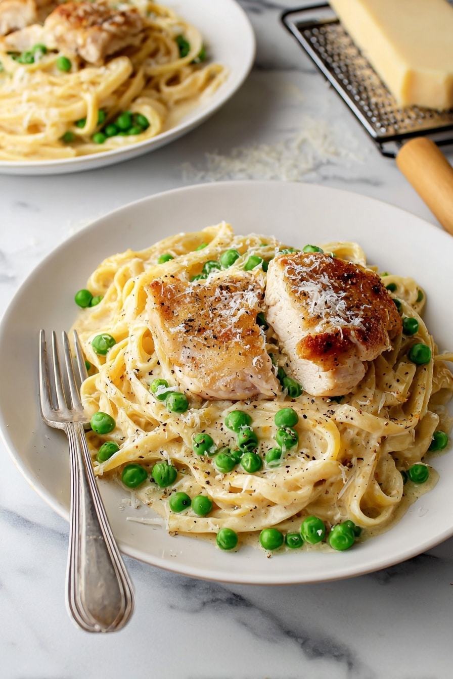 A white plate holds a creamy pasta dish with three slices of golden-brown grilled chicken placed on top. The pasta is mixed with bright green peas and coated in a smooth white sauce. Sprinkled parmesan cheese and black pepper garnish the dish. A spoon and fork rest on the left side of the plate. The plate sits on a white marbled surface, with a beige cloth napkin visible on the right side and a small piece of grated cheese and a grater partially seen toward the top right corner. photo taken with an iphone --ar 2:3 --v 7 - Turkey Alfredo Pasta, creamy turkey pasta, easy turkey pasta recipe, fall comfort food, leftover turkey pasta