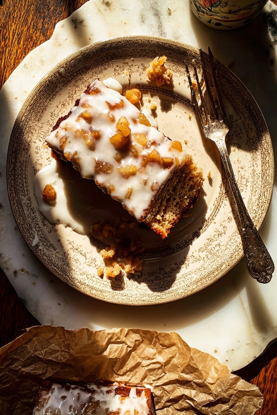 A beige patterned plate holds a rectangular piece of dessert with a rough brown base layer filled with small golden-brown chunks. The top layer is covered in a thick white glaze dripping down the sides and pooling slightly on the plate. There are small scattered bits of the dessert around the main piece, and an old-fashioned silver fork rests diagonally across the plate, partially touching the dessert. The plate sits on a white marbled surface, with sunlight casting strong shadows. A portion of the dessert is also on crumpled brown paper at the bottom of the image, also drizzled with white glaze. Photo taken with an iphone --ar 2:3 --v 7 - Glazed Honeycrisp Apple Fritter Cake, apple fritter dessert, fall apple cake, easy apple cake recipe, Honeycrisp apple recipes