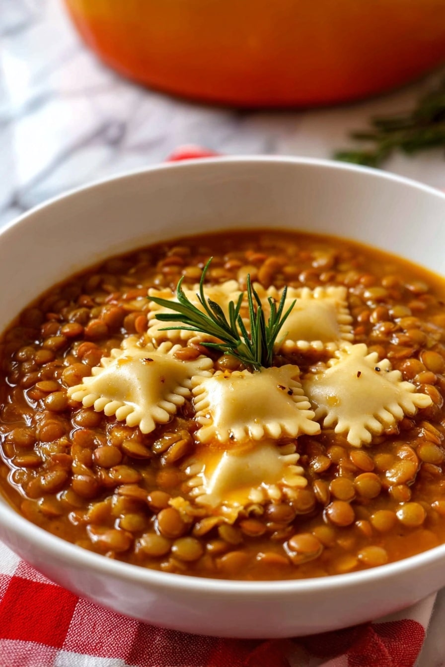 The image shows a white bowl filled with a thick vegetarian lentil soup layered with small, round brown lentils covering the entire surface, mixed with several square pieces of pale yellow pasta scattered evenly on top. The soup has a rich, brownish-orange broth giving the dish a warm color, with a small green rosemary sprig placed in the center as a garnish. The bowl rests on a red and white checkered cloth with a white marbled surface below, and a blurred background hinting at an orange pot. Photo taken with an iphone --ar 2:3 --v 7 - Umbrian Lentil Soup with Pasta, Italian Lentil Soup, hearty Italian soup, rustic lentil and pasta dish, traditional Umbria recipes