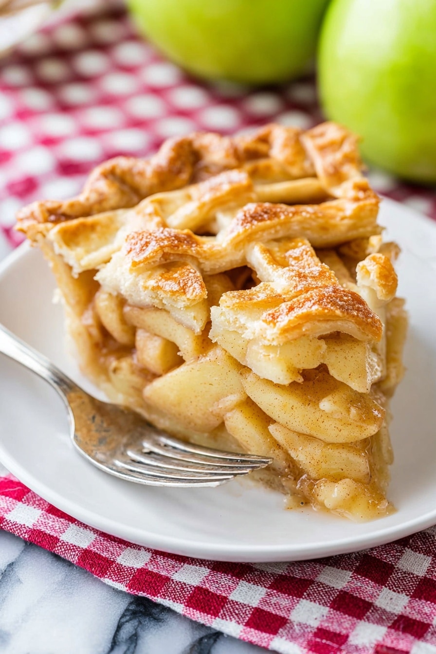 A piece of apple pie sits on a white plate with a silver fork resting beside it. The pie has a golden-brown lattice crust on top, with visible layers of soft, spiced apple slices underneath that appear juicy and tender. The crust edges are slightly crimped and have a flaky texture. Behind the pie, there are two green apples slightly out of focus. The plate is placed on a red and white checkered cloth, all set on a white marbled surface. Photo taken with an iphone --ar 2:3 --v 7 - Apple Pie Classic, Best Apple Pie, Homemade Apple Pie, Flaky Apple Pie Crust, Spiced Apple Pie