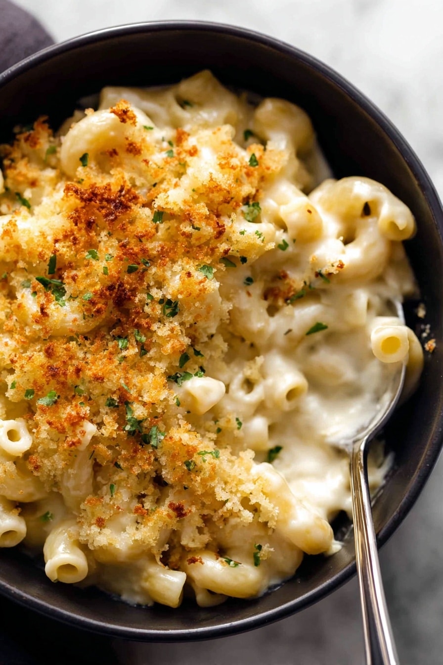 A black bowl holds creamy macaroni and cheese with small tube-shaped pasta covered in a thick white cheese sauce. On top, there is a golden-brown crunchy layer of toasted crumbs with some small green herb pieces sprinkled throughout. A silver spoon is inside the bowl on the right side, resting in the cheese sauce. The bowl is placed on a white marbled surface, and the texture of the pasta is soft and smooth with some crispy topping contrast. Photo taken with an iphone --ar 2:3 --v 7 - Baked Mac and Cheese, baked mac and cheese recipe, cheesy baked mac n cheese, creamy baked pasta, crunchy topping macaroni