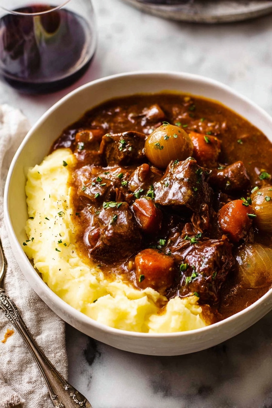 A white bowl filled with a thick layer of creamy mashed potatoes at the bottom, smooth and pale yellow in color. On top, there is a rich layer of dark brown beef stew with chunks of tender beef, orange carrot pieces, and small round light brown onions, all covered in a glossy, thick brown gravy. Small green herbs are sprinkled on top, adding a bit of color contrast. The background is a white marbled texture. Photo taken with an iphone --ar 2:3 --v 7 - Beef Bourguignon, Beef Burgundy, classic French beef stew, slow cooker beef stew, hearty beef bourguignon recipe