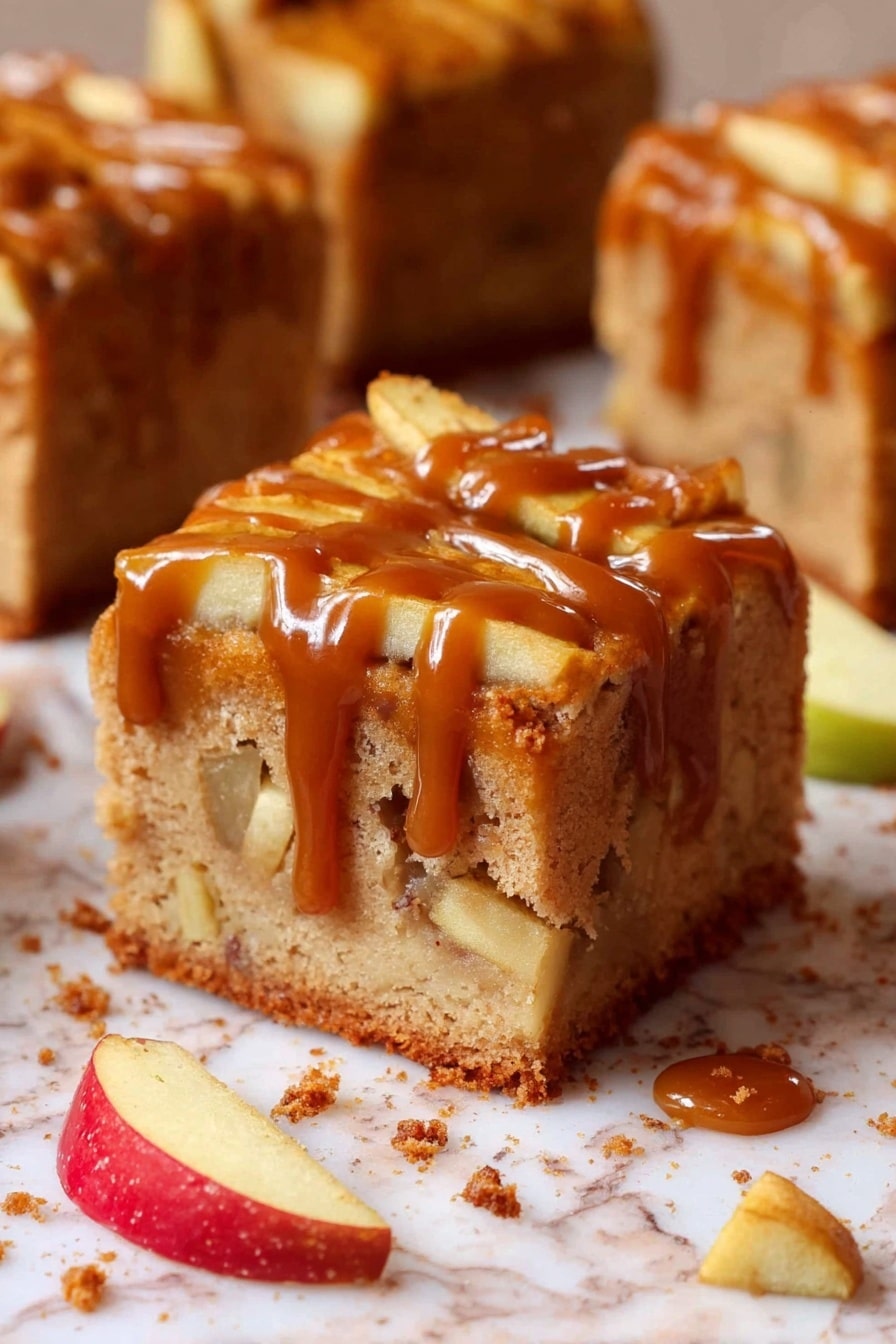 A thick square slice of apple cake shows two visible layers: the bottom is a light brown soft cake base with apple chunks inside, and the top layer is covered with thin apple slices partially lengthened by a messy layer of glossy caramel sauce dripping down the sides. The cake sits on white marbled surface sprinkled with crumbs, small apple chunks, and thin apple slices nearby. The background shows more similar cake slices out of focus. Photo taken with an iphone --ar 2:3 --v 7 - Caramel Apple Cake,Apple Cake with Caramel,Autumn Dessert Recipes,Easy Apple Cake,Fall Baking Ideas