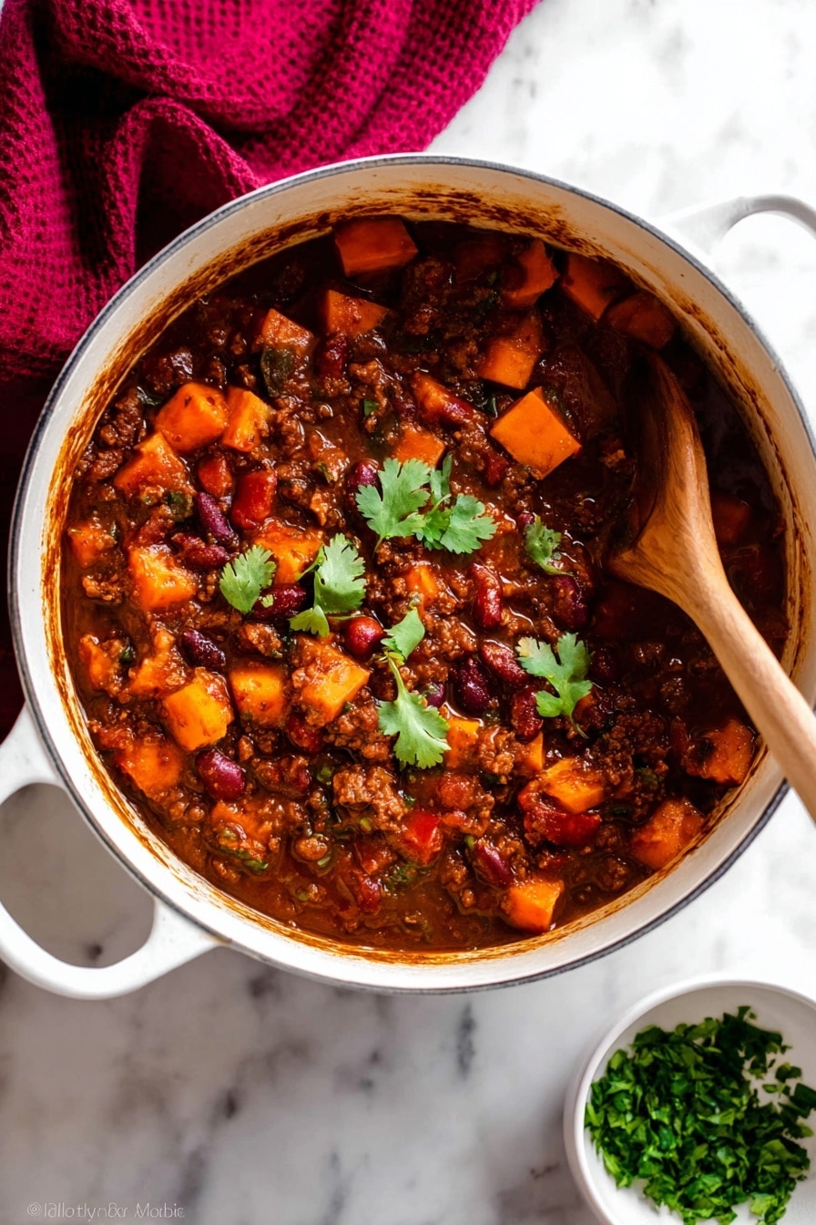 A white pot filled with thick stew that has three main layers: a dark brown sauce base, chunky orange sweet potato pieces, and visible red and brown beans mixed with ground meat; a few green cilantro leaves float on top near the center for color contrast. A wooden spoon is partially dipped on the right side, stirring the stew, showing the dense texture and rich sauce coating all ingredients. The pot rests on a white marbled surface with a dark red cloth draped in the upper left corner and a small white bowl filled with chopped green herbs placed near the bottom right. Photo taken with an iphone --ar 2:3 --v 7 - Vegetarian Pumpkin Chili, hearty vegetarian chili, pumpkin chili recipe, vegetarian pumpkin soup, easy healthy chili