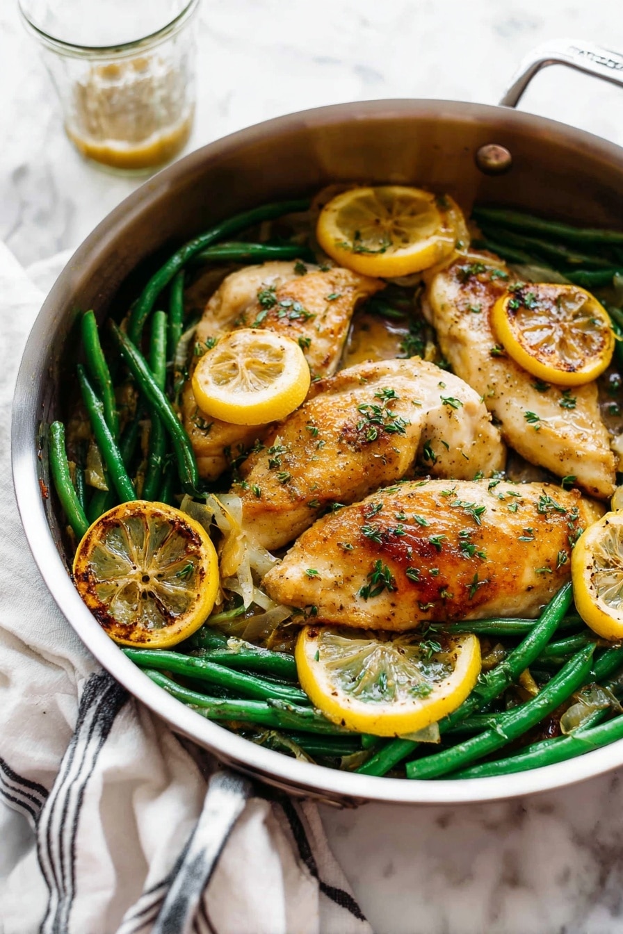 A round silver pan holds a dish with three light golden brown cooked chicken pieces on top. Underneath and around the chicken are bright green beans and several round slices of cooked lemon that are golden and slightly charred on the edges. The chicken is sprinkled with small green herb pieces and has a slightly shiny sauce coating parts of it. The pan is placed on a white marbled surface, with a white cloth with black stripes in the back left and a glass cup with some sauce behind the pan. Photo taken with an iphone --ar 2:3 --v 7 - Garlic Lemon Butter Chicken Skillet, easy chicken skillet recipes, quick chicken dinner, flavorful chicken recipes, weeknight chicken ideas