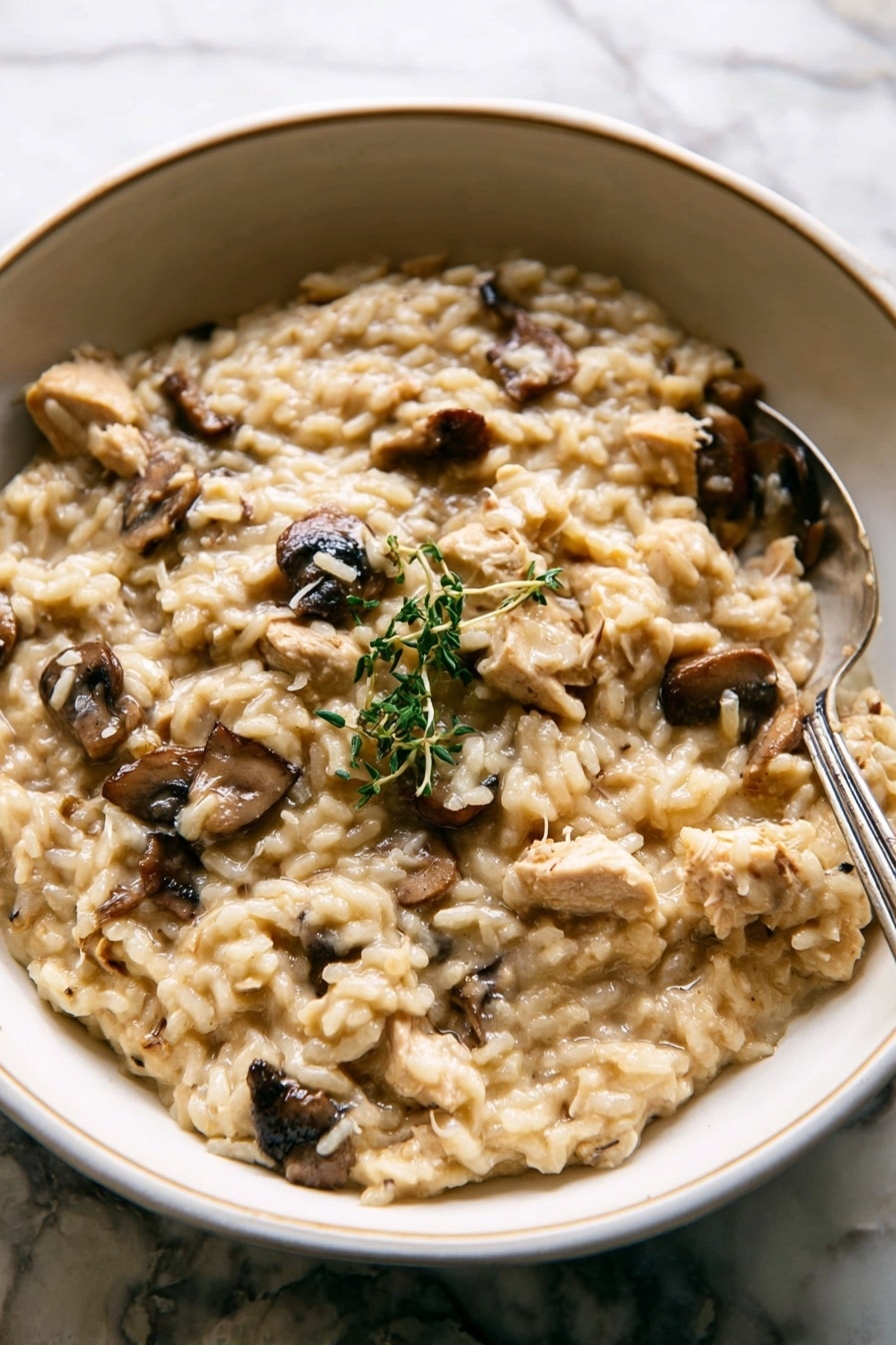 A close-up of creamy risotto served in a white bowl with a pale green-blue inner glaze texture. The risotto has a light beige color with soft, plump rice grains and visible chunks of light brown chicken and dark brown mushrooms. A small green herb sprig rests on top as garnish. A silver fork sits on the right side partially stuck into the risotto. The background is a white marbled texture with a few out-of-focus green herb stems visible at the top. photo taken with an iphone --ar 2:3 --v 7 - Chicken Mushroom Risotto with Thyme, Chicken Mushroom Risotto, Creamy Mushroom Risotto, Easy Chicken Risotto, Thyme Infused Risotto