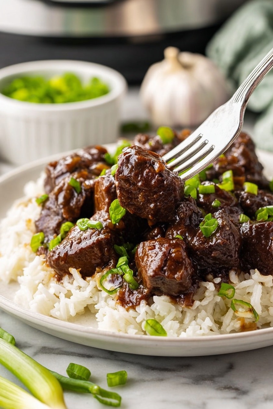 The dish shows a single white plate on a white marbled table, holding two main layers: the bottom layer is white rice with some chopped green onions scattered on top, and the top layer is dark brown beef chunks covered in a shiny glaze, also garnished with green onions. A silver fork pierces one beef chunk in the center of the plate, lifting it slightly above the rest. In the background, a whole garlic bulb and a small white bowl with more green onions are partially visible, adding to the kitchen setting. Photo taken with an iphone --ar 2:3 --v 7 - Honey Garlic Steak Bites, Honey Garlic Steak Bites recipe, Easy Steak Bites, Quick Dinner Ideas, Delicious Steak Bites