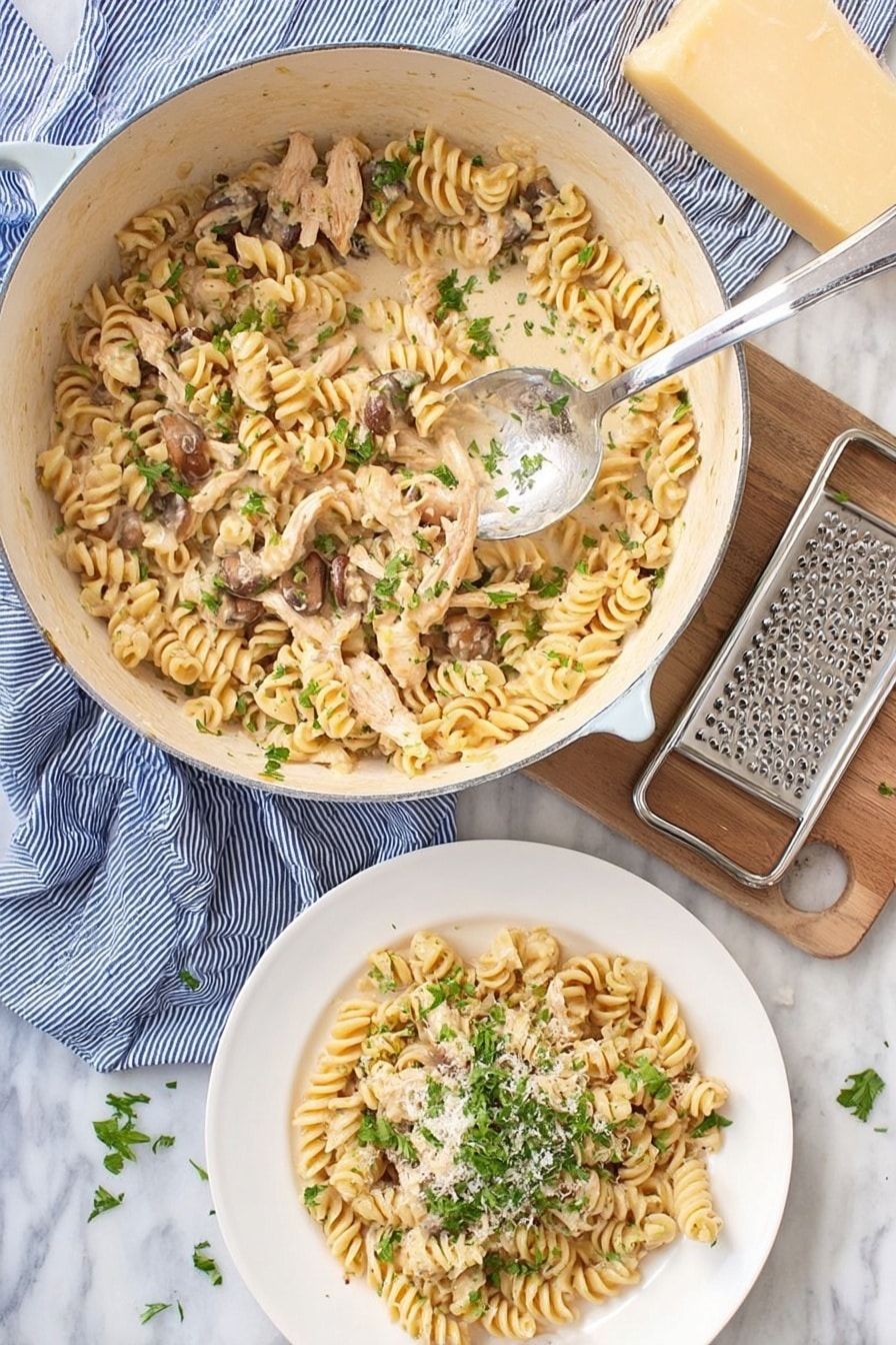 A white pot filled with creamy cooked rotini pasta mixed with light brown cooked chicken strips and small brown mushrooms, sprinkled with fresh green chopped herbs on top, a silver spoon rests inside the pot lifting some pasta. Below the pot, there is a white plate with a serving of the same pasta topped with more green herbs and a light sprinkle of grated cheese. To the side, a block of light yellow cheese and a metal grater rest on a blue striped cloth, all placed on a white marbled surface. photo taken with an iphone --ar 2:3 --v 7 - Creamy Turkey Pasta, leftover turkey pasta, quick turkey pasta, easy creamy pasta, Thanksgiving turkey recipes