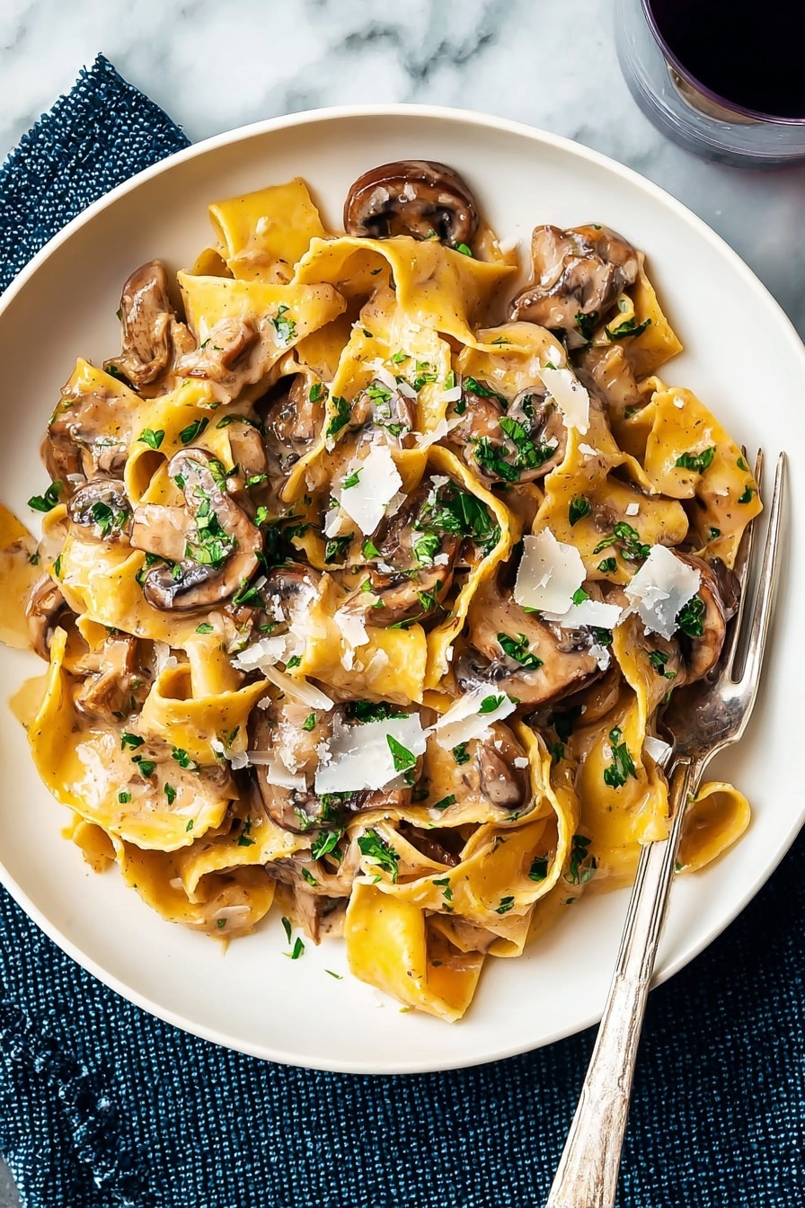 A white plate holds a serving of wide, yellow pasta ribbons cooked in a light brown creamy mushroom sauce. On top, there are several brown, slightly browned mushroom slices mixed throughout the pasta, adding a smooth texture. Bright green chopped herbs are sprinkled over the dish, giving a fresh contrast. Light shavings of white cheese are scattered on top, melting slightly into the sauce. A silver fork rests on the edge of the plate, and the plate is placed on a white marbled surface with a dark blue textured cloth beneath one side. Photo taken with an iphone --ar 2:3 --v 7 - Vegetarian Mushroom Stroganoff, easy vegetarian stroganoff, creamy mushroom pasta, plant-based stroganoff recipe, quick mushroom dinner