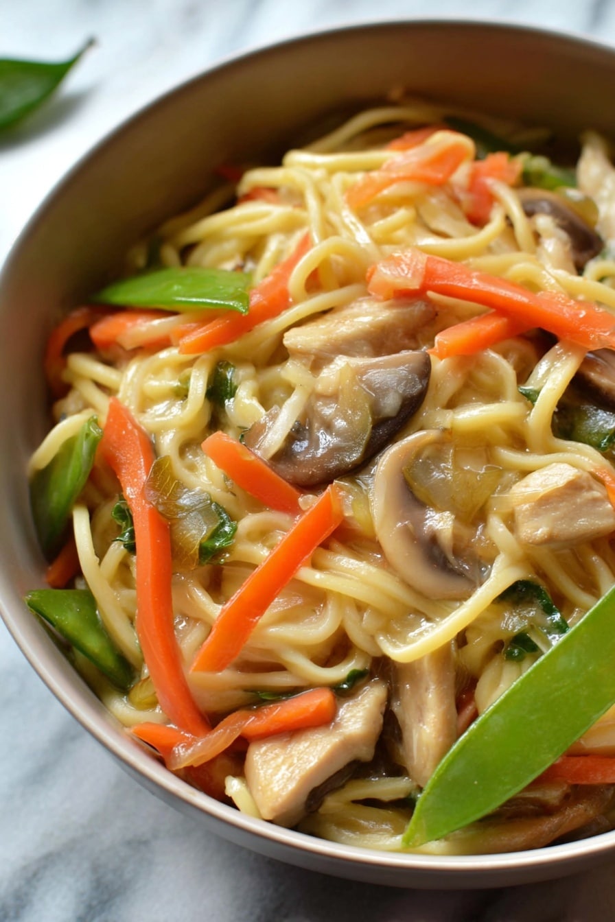 A close-up shot of a round white bowl filled with a noodle dish that has three main visible layers. The base layer consists of light yellow noodles that look soft and slightly shiny. Mixed in and on top of the noodles are bright orange thin carrot strips, pale green sliced snow peas, and light brown sliced mushrooms. Scattered throughout are small pieces of light brown cooked chicken or tofu, adding texture contrast. The background shows an out-of-focus white marbled surface, giving the dish a clean and fresh look. Photo taken with an iphone --ar 2:3 --v 7 - Instant Pot Chicken Lo Mein, easy chicken lo mein, quick Chinese stir-fry, healthy instant pot noodles, one-pot lo mein