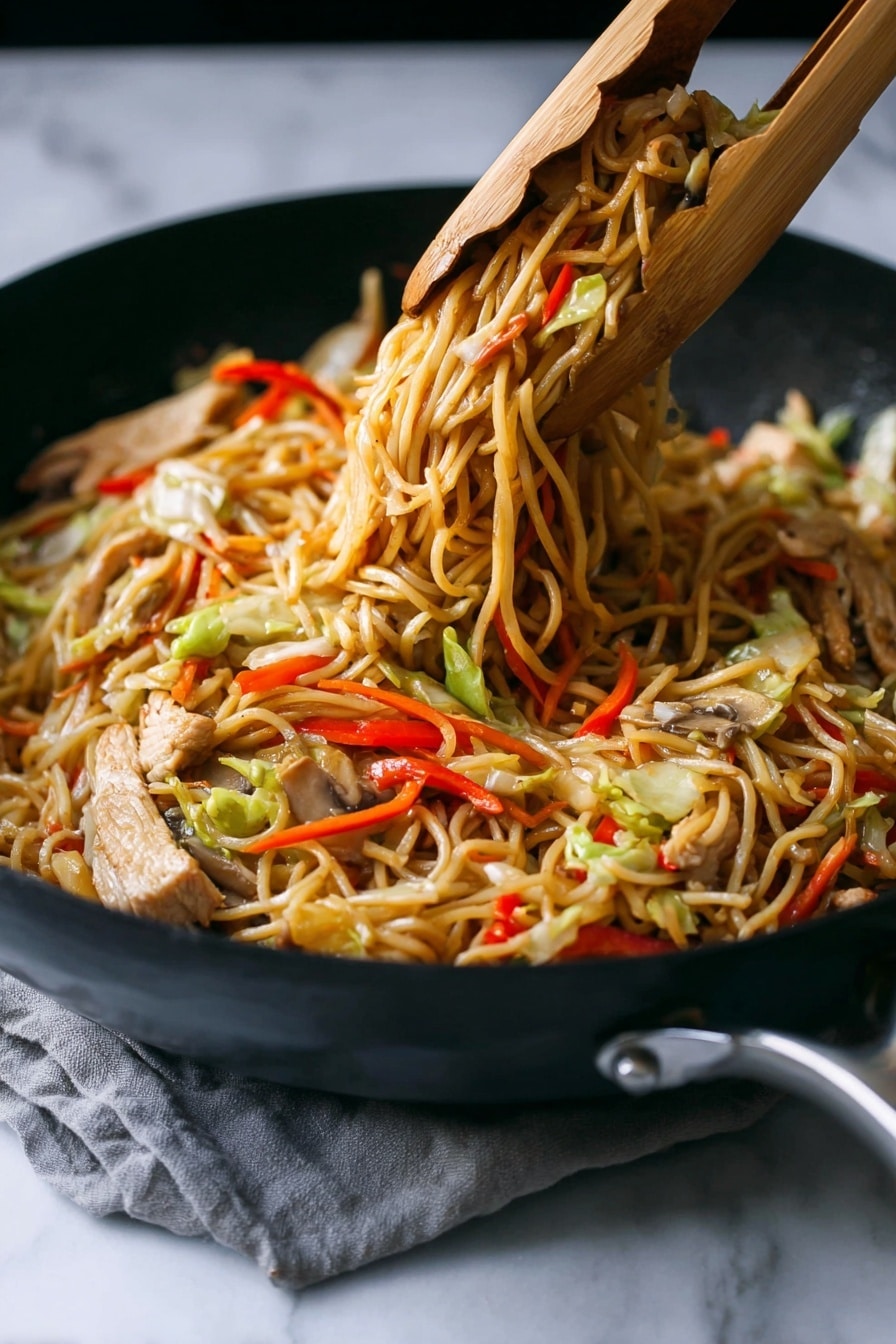 A close-up of a black skillet filled with cooked stir-fried noodles lifted by wooden tongs, showing three main layers: a base layer of thin, light brown noodles tangled together; mixed throughout are slices of light beige cooked meat and strips of vegetables including red bell peppers, pale green cabbage, thin orange carrot sticks, and light brown mushrooms. The noodles have a slightly shiny texture, and the colors of the vegetables add bright, fresh contrast. The skillet rests on a white marbled surface with a subtle grey cloth partially visible under the handle. photo taken with an iphone --ar 2:3 --v 7 - Chicken Yakisoba Stir-Fry, Chinese stir-fry recipes, quick Asian noodle dishes, homemade yakisoba, veggie stir-fry recipes